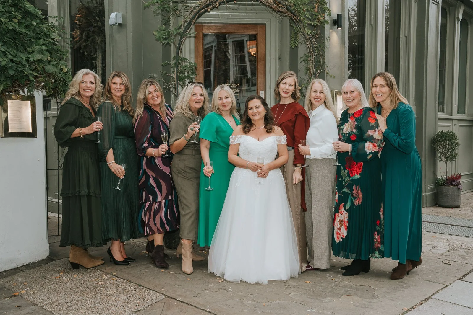  Bride and wedding guests holding champagne flutes outside the foliage-framed entrance to The Phene pub in Chelsea. 