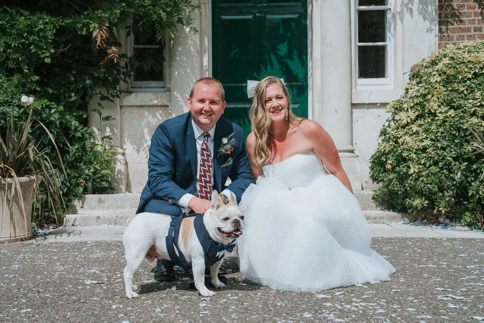  Newlyweds crouching beside their bulldog in front of the green entrance door at Morden Park House. 