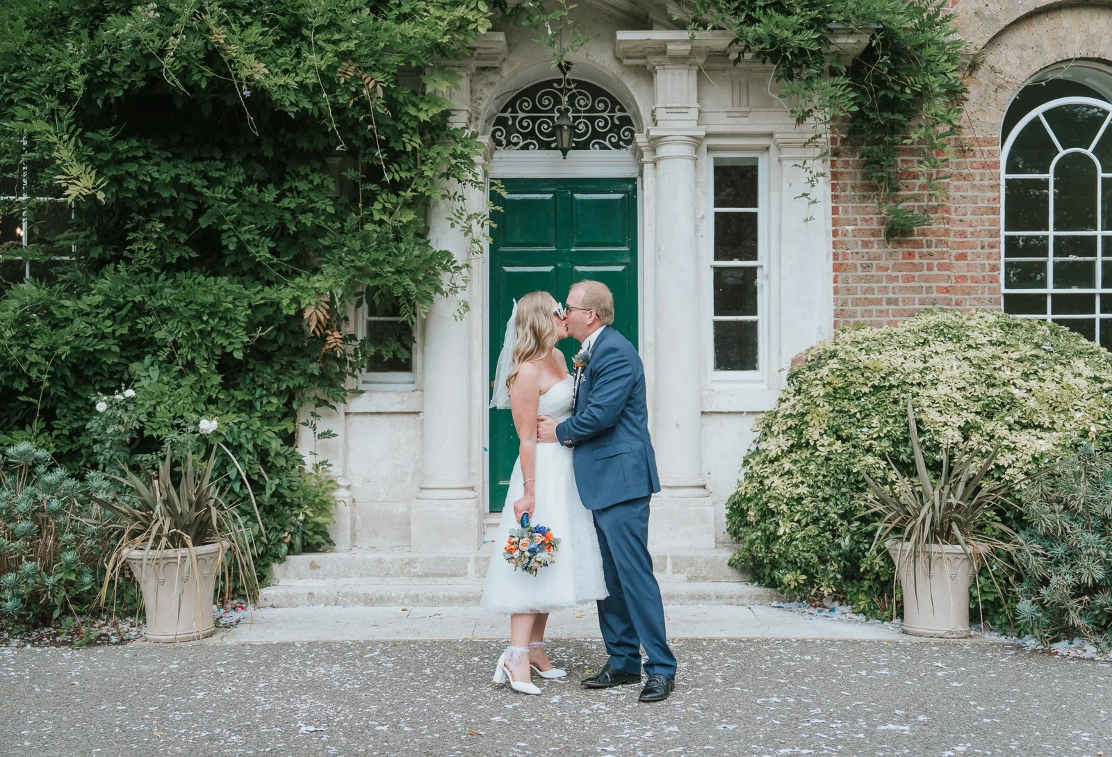  Bride and groom kissing beside the green entrance door at Morden Park House. 