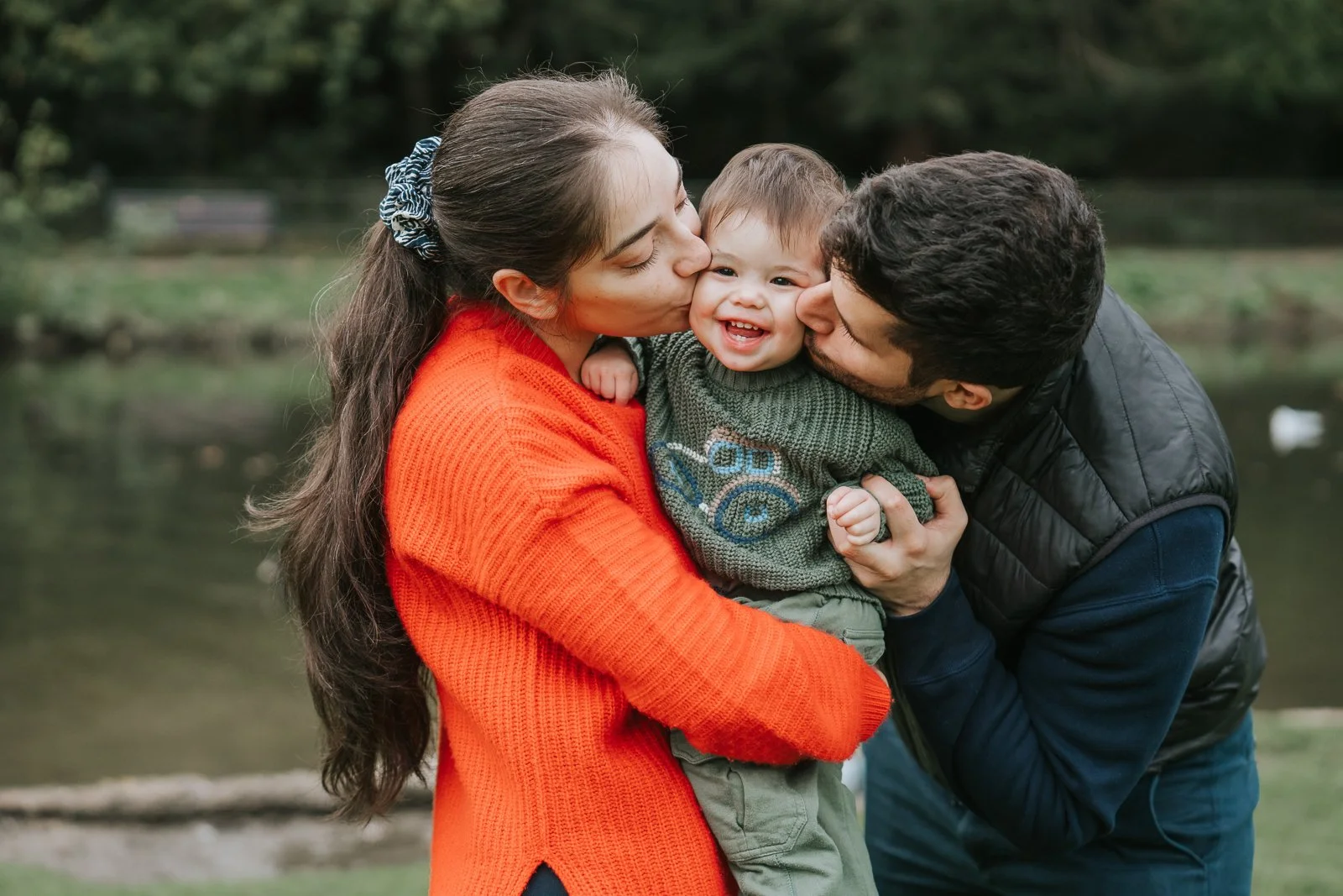 A mum and dad kiss their young son during a family photoshoot.