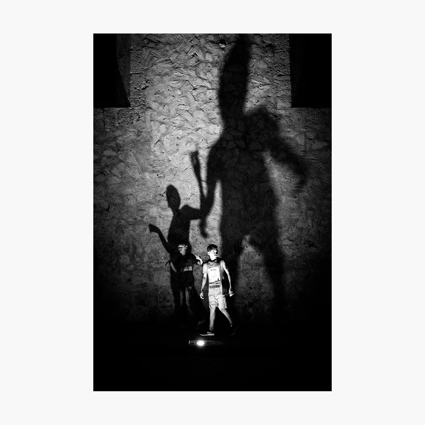 @harrywedmonds Cartagena, Colombia, South America December 2017 I noticed shadows rising up the side of this building every now and then, looming out of the surrounding darkness. It immediately captured my attention. But I wasn’t happy with just a vague profile of a person passing. Another case of patience and perseverance in street photography: These boys eventually appeared, chatting away and gesticulating at something behind them just as they passed the light source. It’s a shot that really benefited from a wider angle lens, making room for those enormous shadows. Photographed using the FujiFilm X-T2 and the XF35 F2 WR .