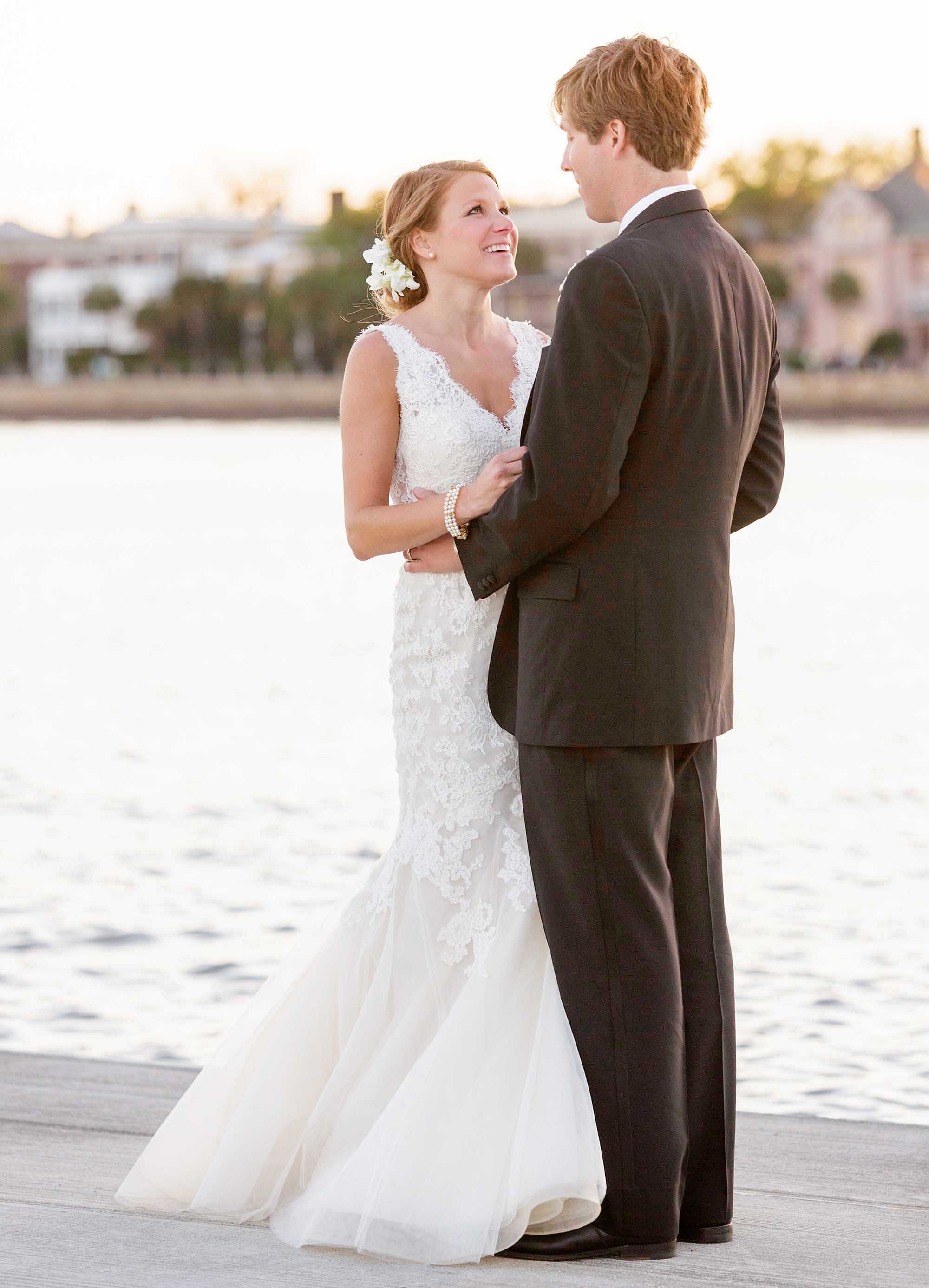 A newly married couple hug on a dock.