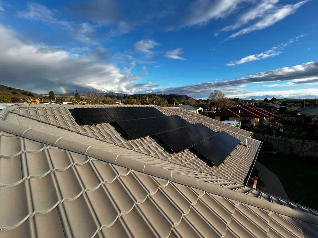 Residential roof with multiple black solar panels installed, under a partly cloudy sky with some sunlight.
