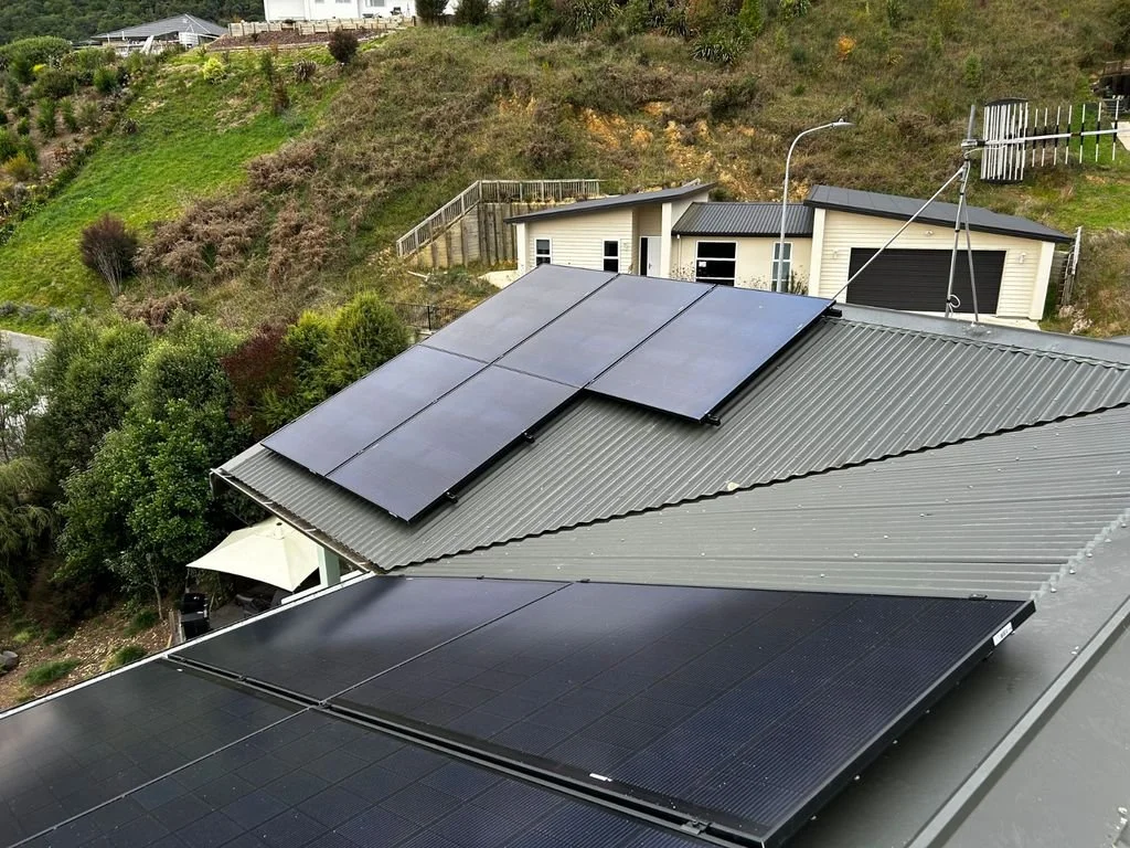Solar panels installed on the roof of a house with a hillside and neighboring garage in the background.
