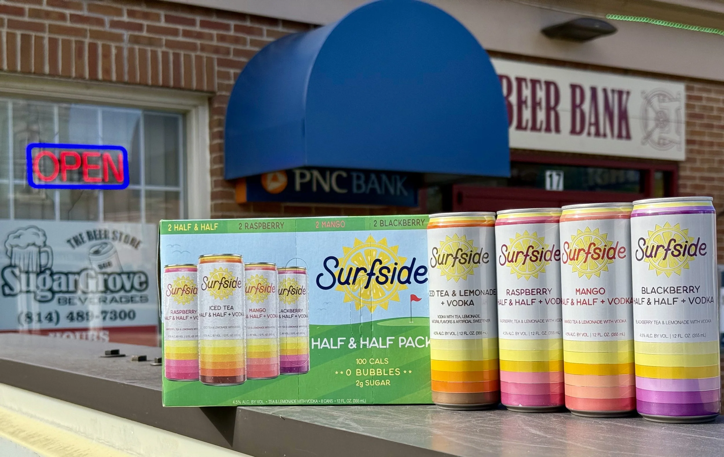 Display of Surfside brand flavored sparkling water cans with raspberry, mango, and blackberry flavors, and a green box of half-and-half flavored sparkling water