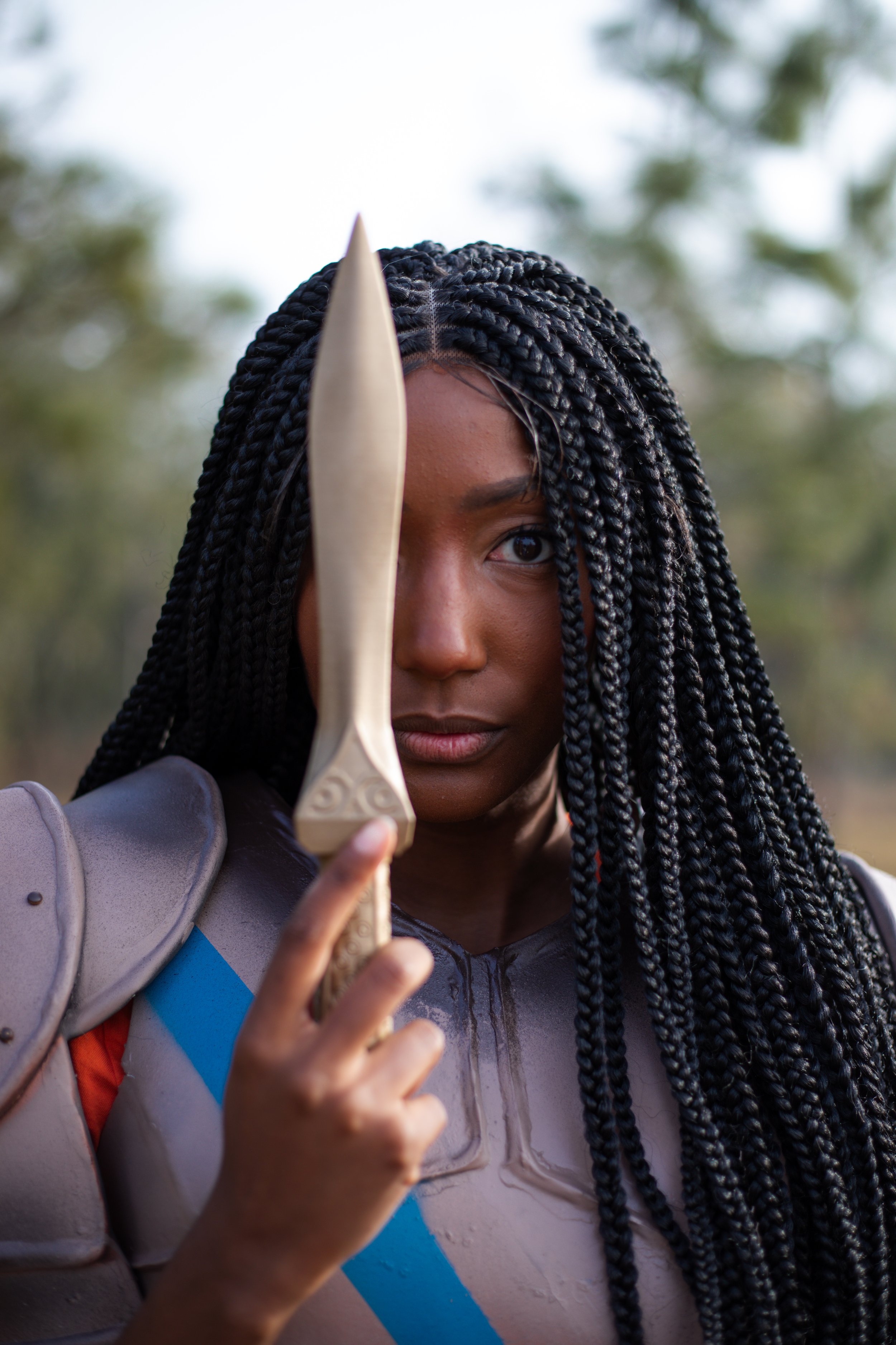 LiteraryPrincess Cosplaying Annabeth Chase in an orange camp half-blood t-shirt, similar to how she appears played by Leah Sava Jeffries in the pjo tv series. They are holding a knife in front of their face, covering one eye