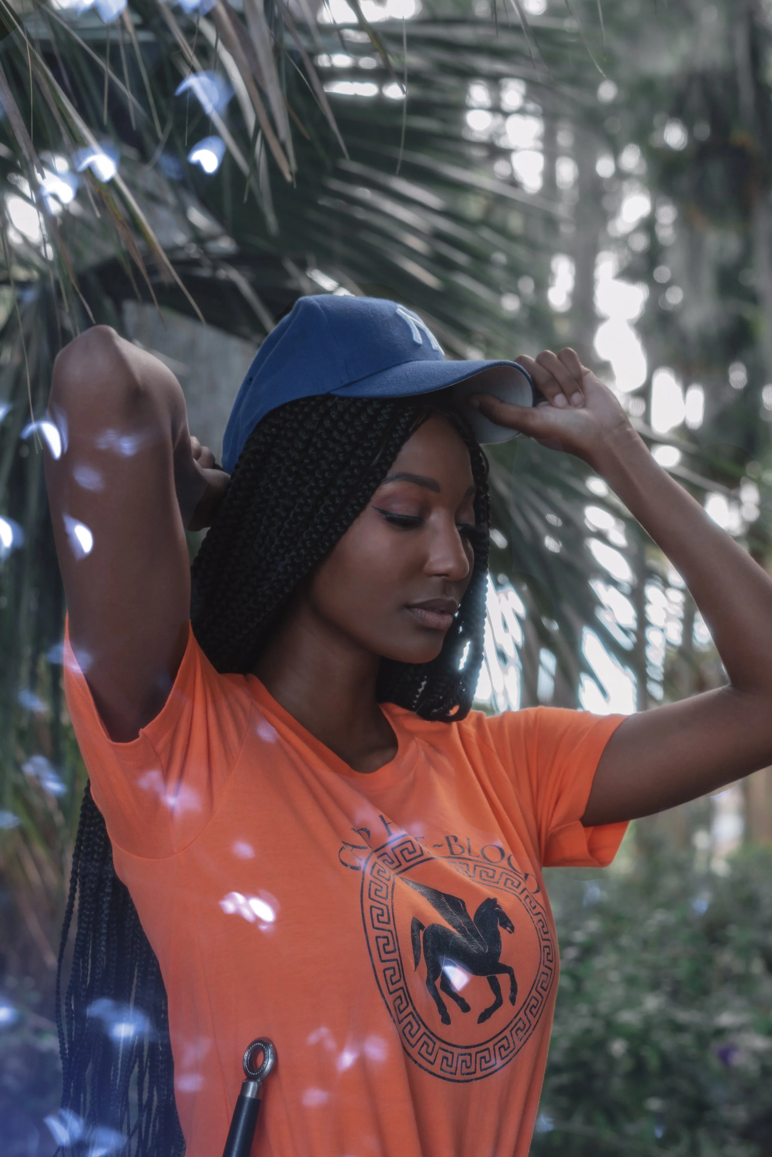 LiteraryPrincess Cosplaying Annabeth Chase in an orange camp half-blood t-shirt, similar to how she appears played by Leah Sava Jeffries in the pjo tv series. They are putting on a yankees cap and looking pensive