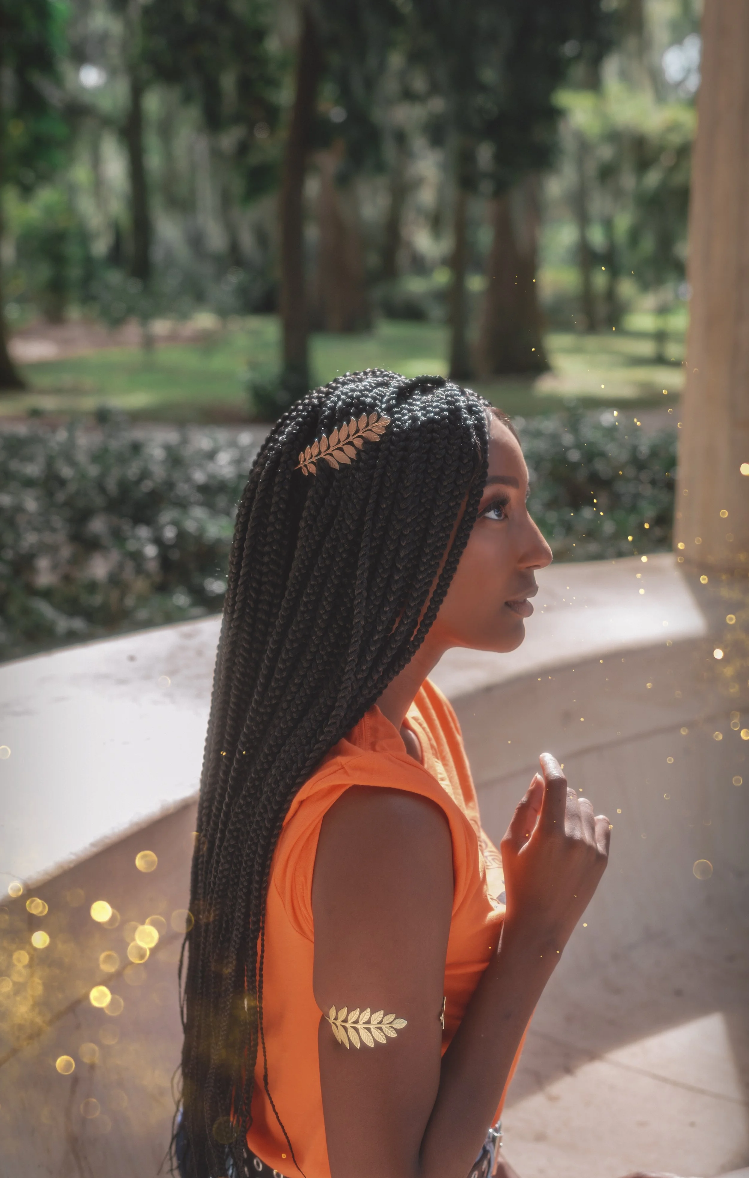 LiteraryPrincess Cosplaying Annabeth Chase in an orange camp half-blood t-shirt, similar to how she appears played by Leah Sava Jeffries in the pjo tv series. They have gold laurel leaf jewelry on their arm and in their hair, and look ethereal