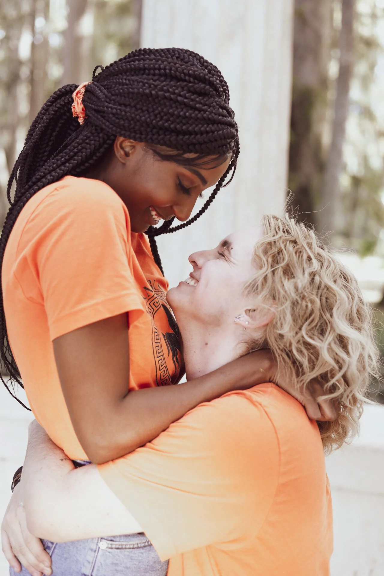 LiteraryPrincess Cosplaying Annabeth Chase in an orange camp half-blood t-shirt, with a blonde percy jackson cosplayer in the same; the percy is lifting the annabeth and they're grinning at each other