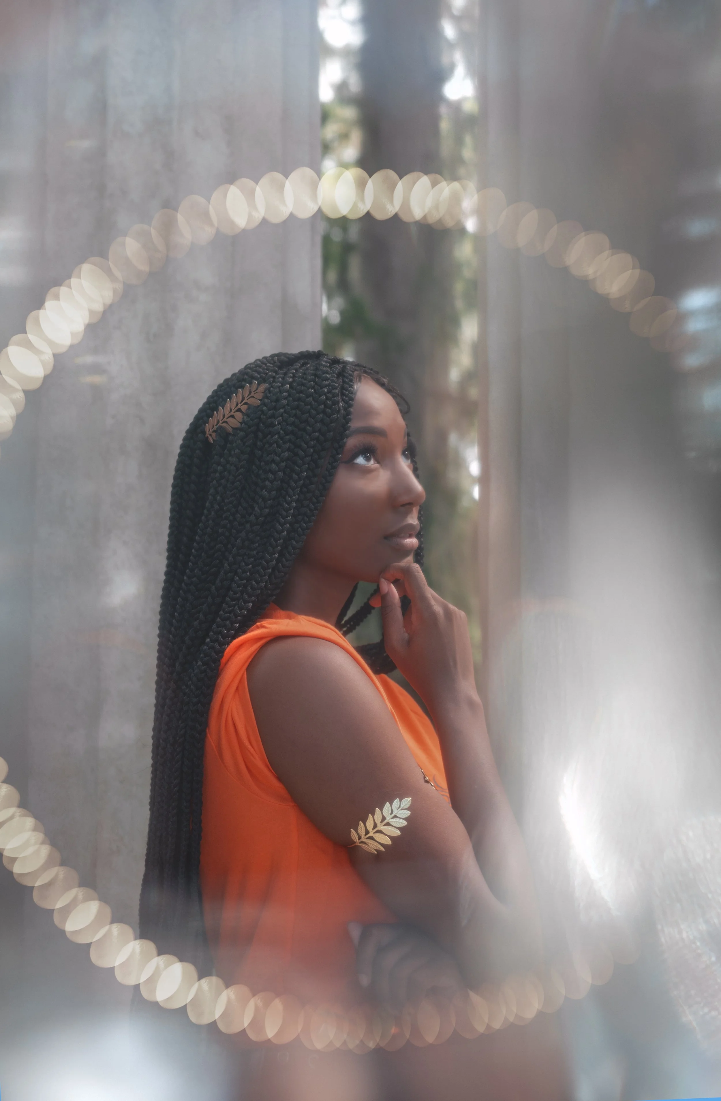 LiteraryPrincess Cosplaying Annabeth Chase in an orange camp half-blood t-shirt, similar to how she appears played by Leah Sava Jeffries in the pjo tv series. They have gold laurel leaf jewelry on their arm and in their hair, and look ethereal