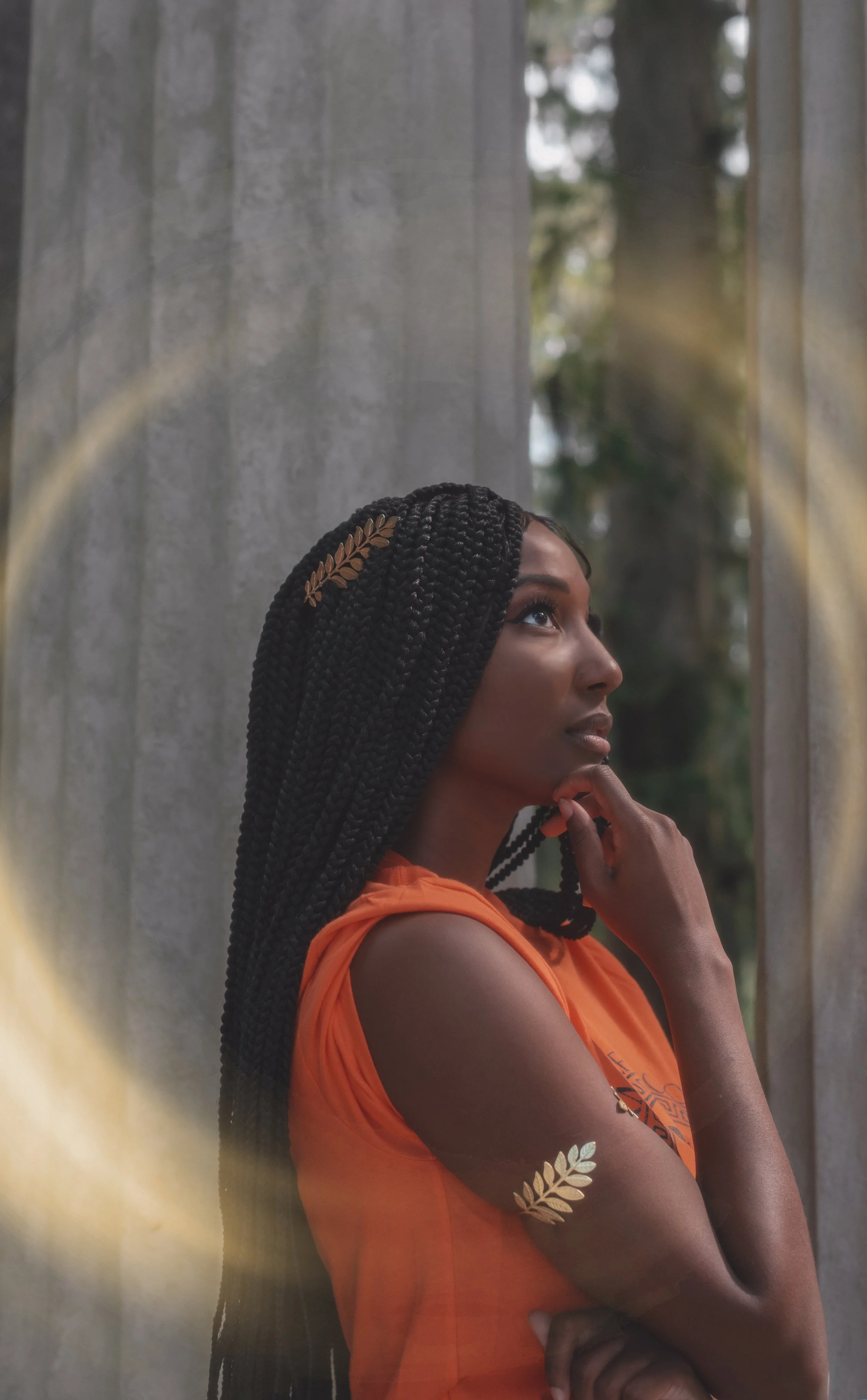 LiteraryPrincess Cosplaying Annabeth Chase in an orange camp half-blood t-shirt, similar to how she appears played by Leah Sava Jeffries in the pjo tv series. They have gold laurel leaf jewelry on their arm and in their hair, and look ethereal