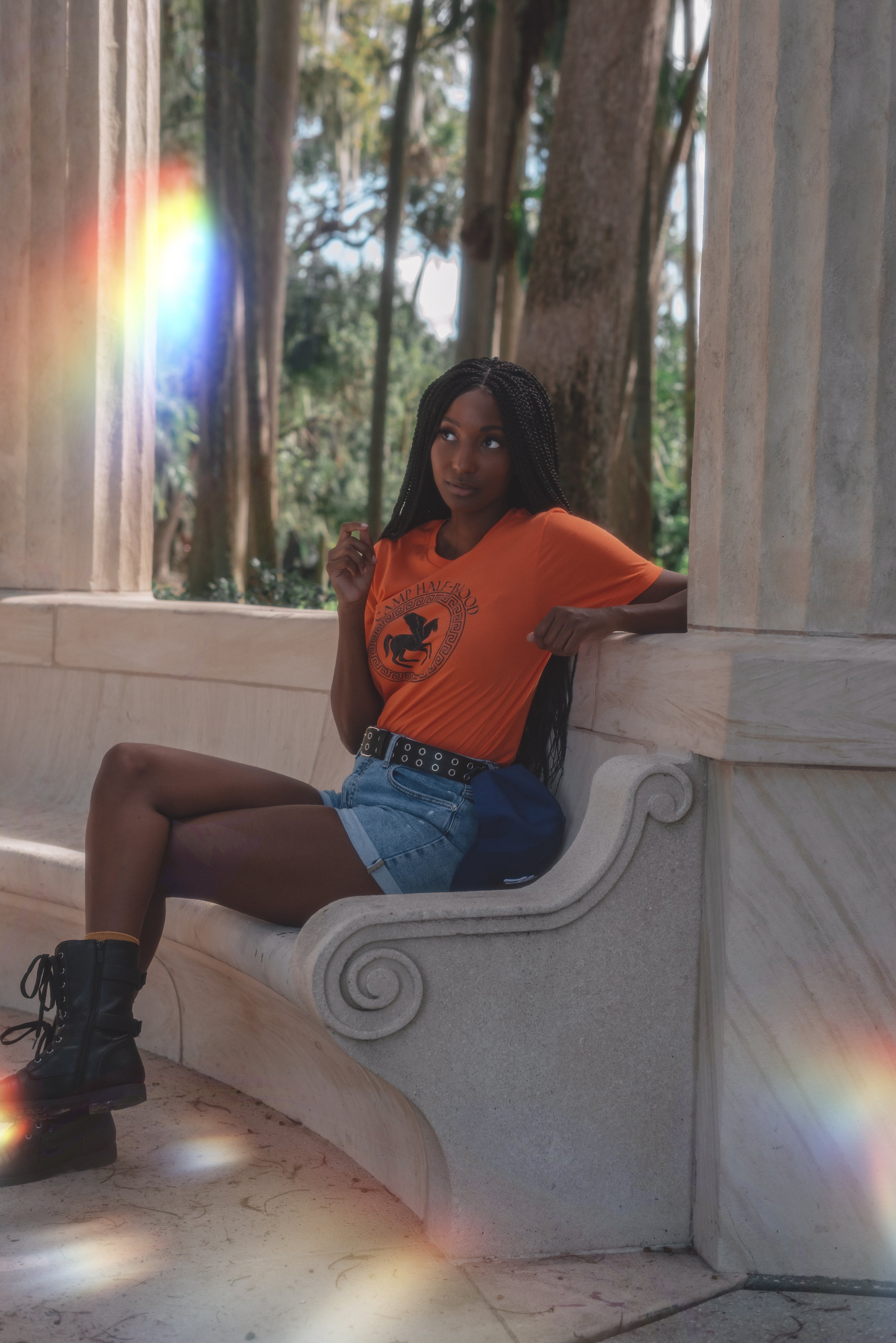 LiteraryPrincess Cosplaying Annabeth Chase in an orange camp half-blood t-shirt, similar to how she appears played by Leah Sava Jeffries in the pjo tv series. sitting in a white marble grecian style structure against a pillar.