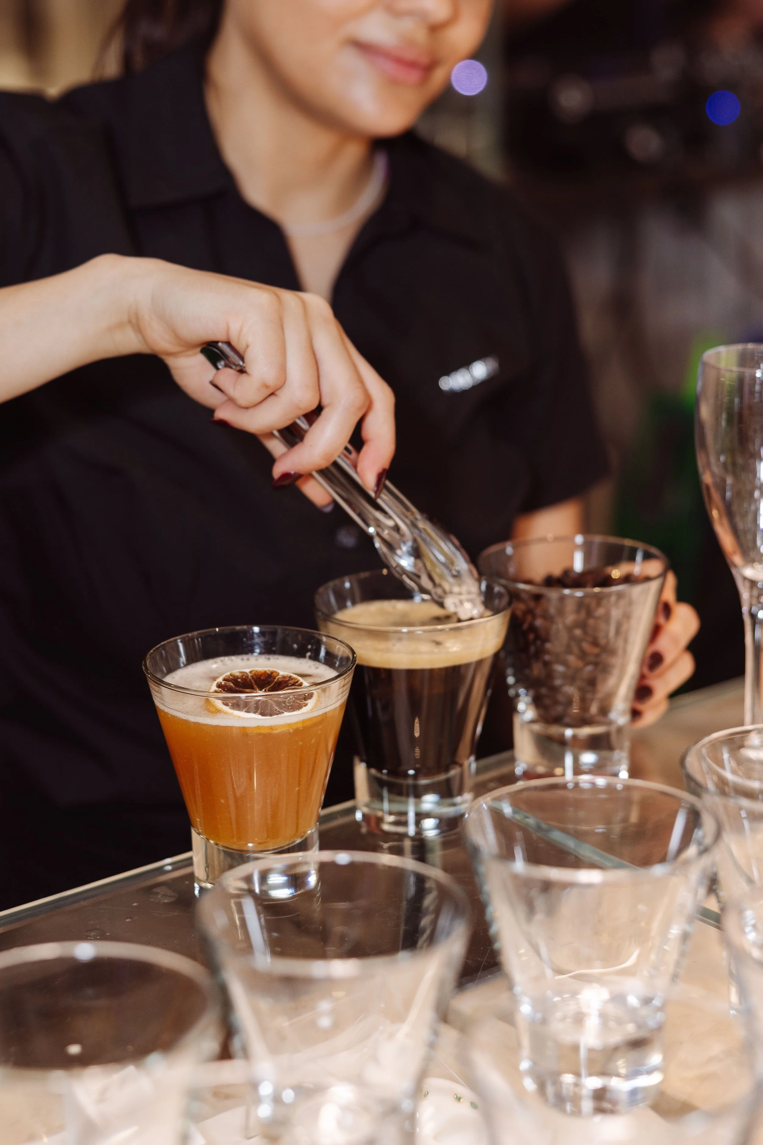 A bartender preparing coffee and cocktail drinks at a bar, with several glasses containing different beverages on the counter.