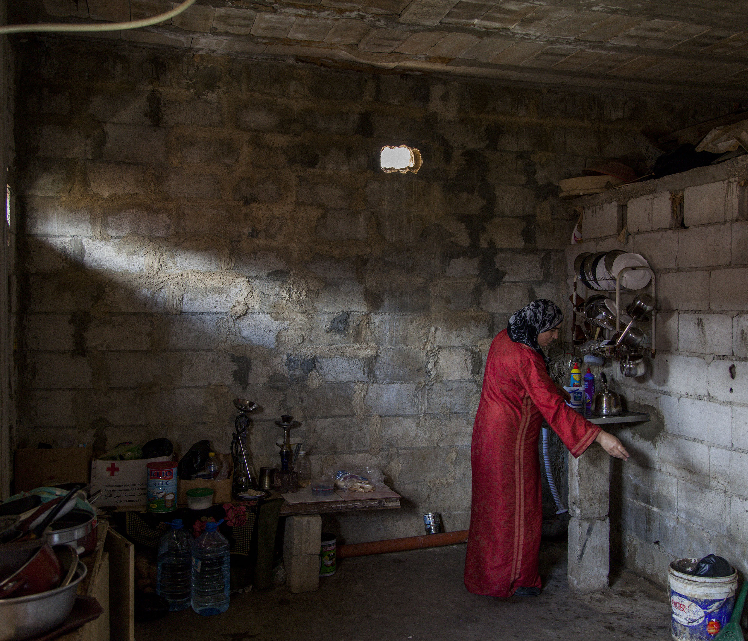  40-year-old Khitan does some washing up in the kitchen of the unfinished building where she lives with her Injured son Rabih and several other Syrian families in Tripoli, Lebanon. 