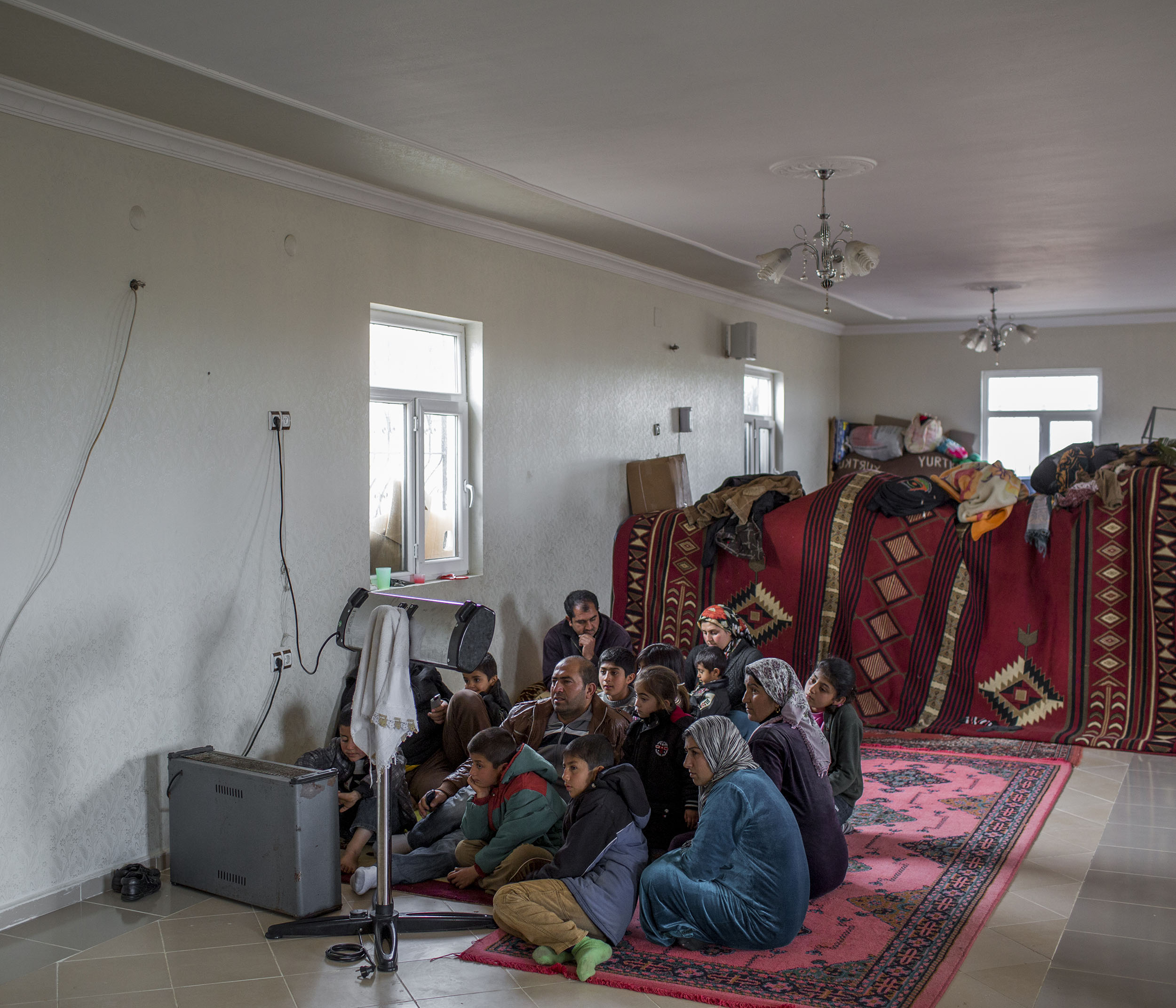  A family of Syrian refugees from Kobane huddle around the heater while watching TV in the unfinished building where they have found refuge in Turkey. 