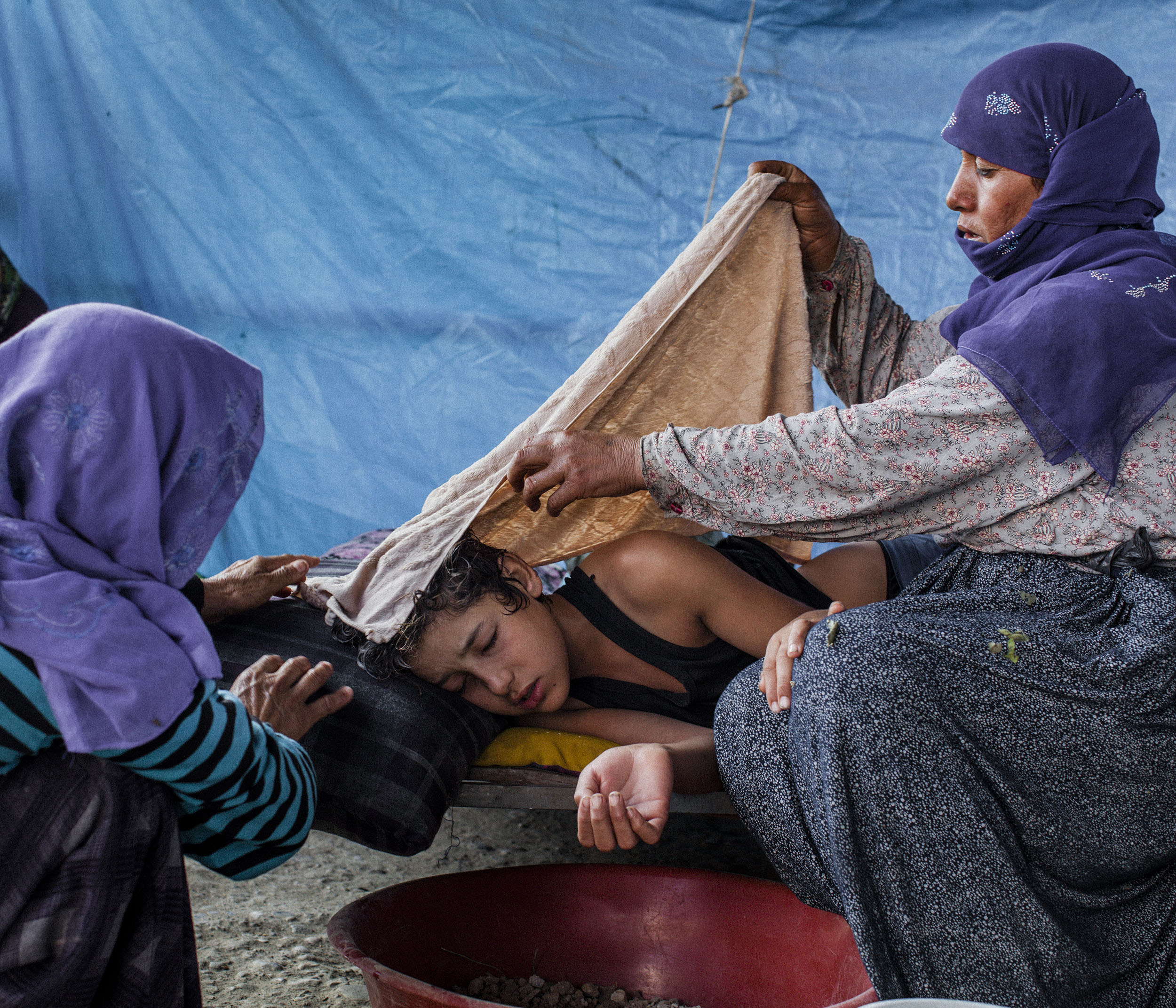  Nizal (14) is tended to by his mother (right) and a relative, after falling ill with a high fever and vomiting. The family were living in a small tented area on the outskirts of Adana in southern Turkey after fleeing Syria 5 months before. 