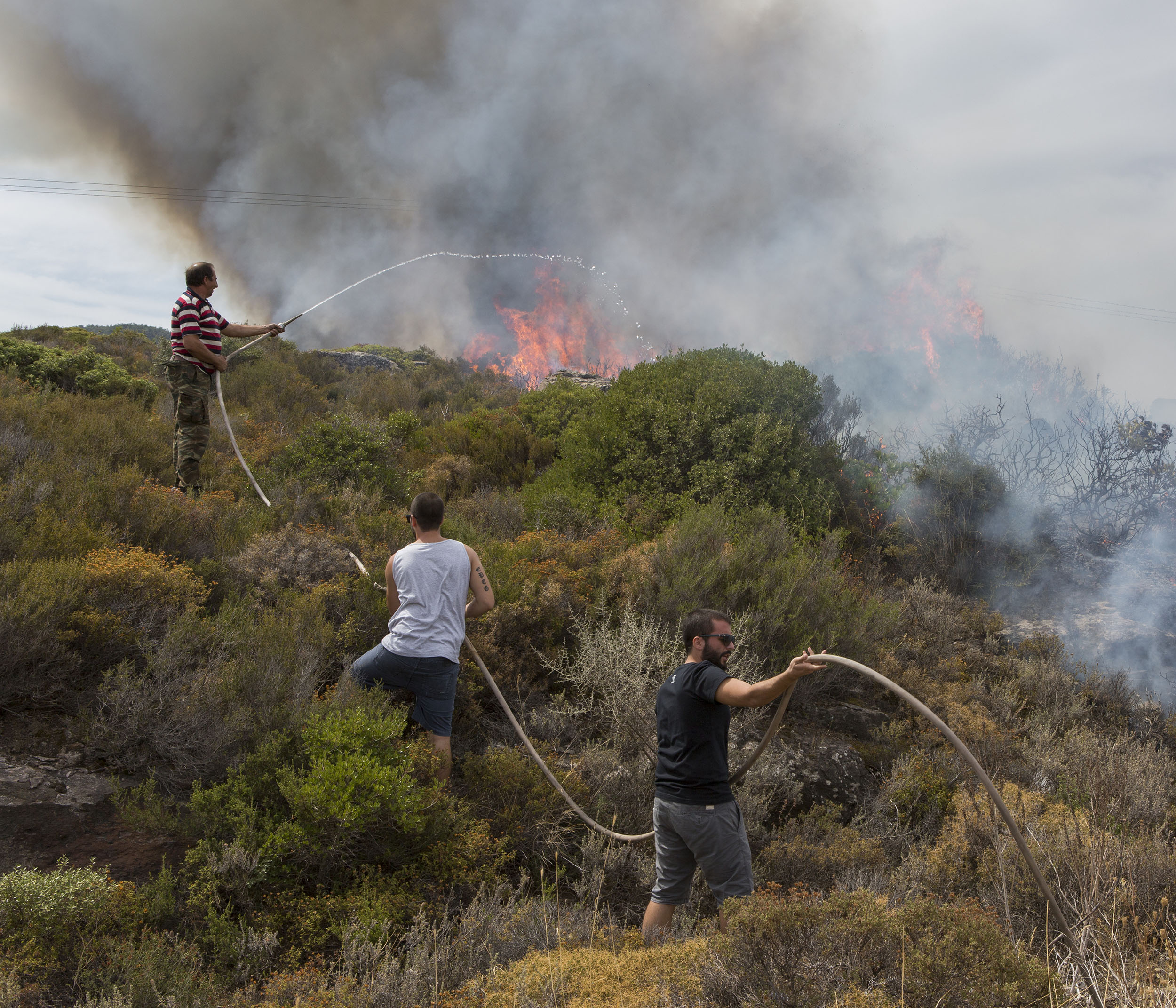 Local Greek men from a volunteer fire crew try to put out a blaze on the coastal road connecting the North of Lesvos to the capital Mytilini. Many of the thousands of refugees who are landing on the island have to walk the 65km route in order to get