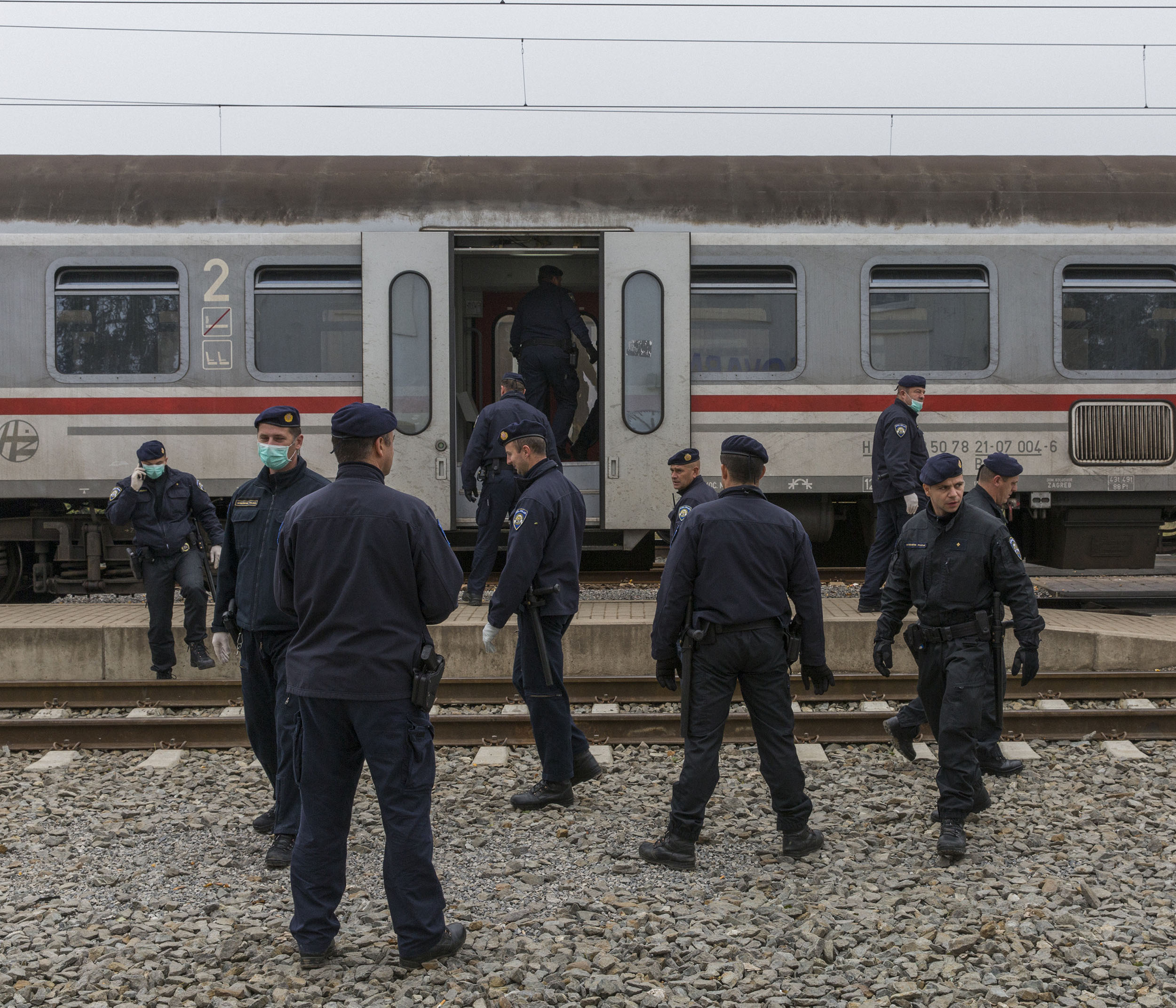 Syrian refugees wait to deapart on trains from Croatia to the Slovenian border while Croatian police look on.