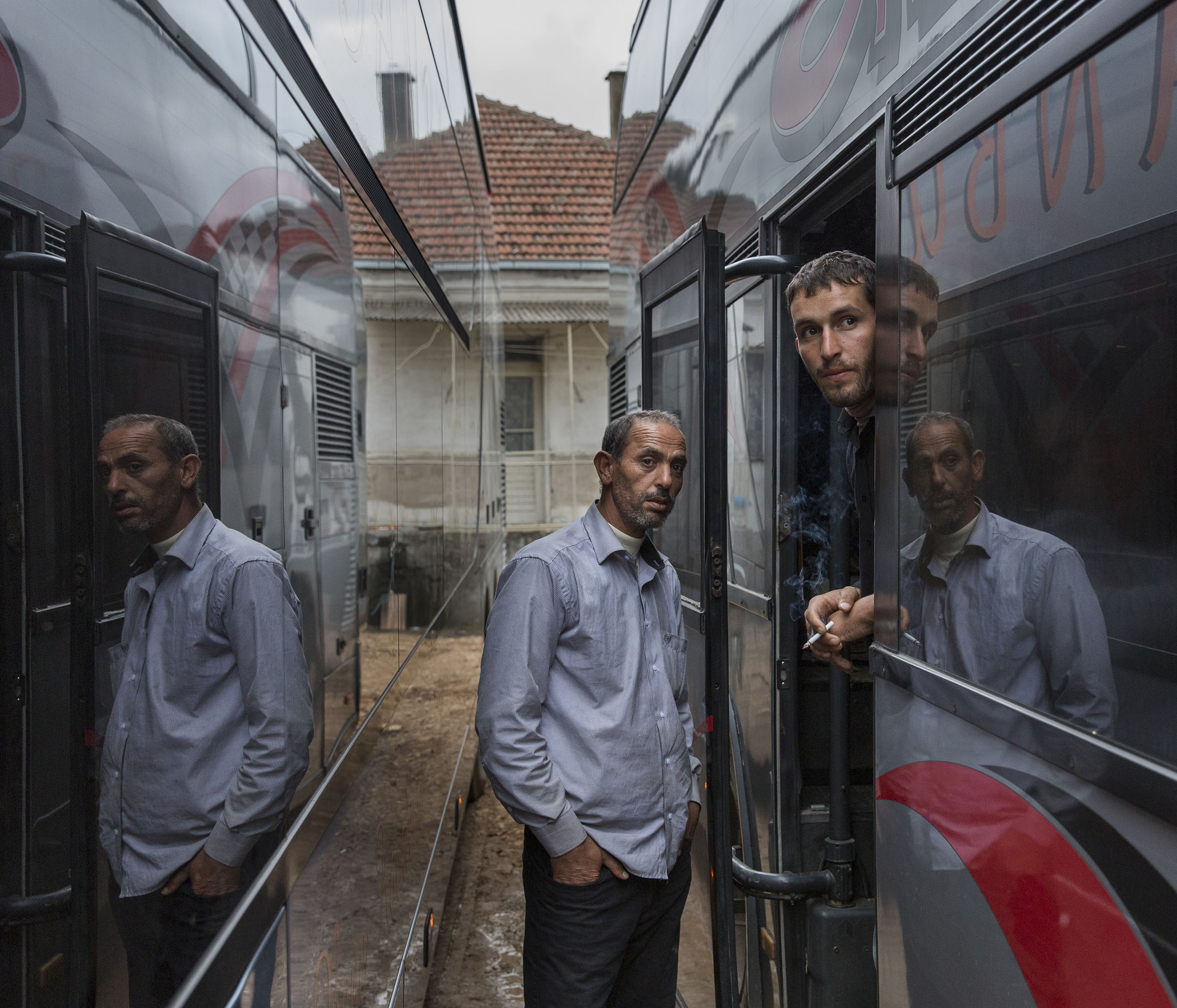 Syrian refugees smoke between rows of buses while they wait for theirs to depart from the Serbian border town of Presevo for the North East border with Croatia.