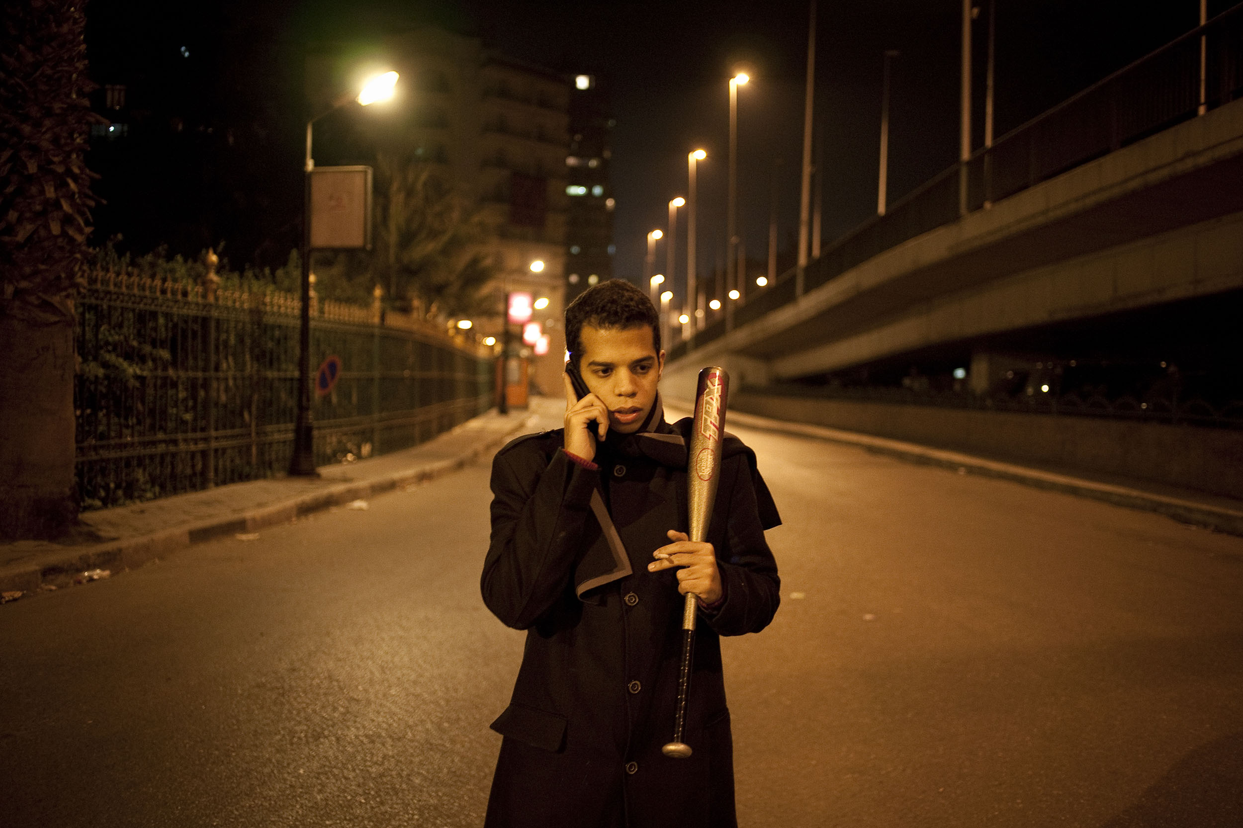  A young man guards the middle class neighbourhood of Zamalek from looters and gangs as he talks on a mobile phone holding a baseball bat.  