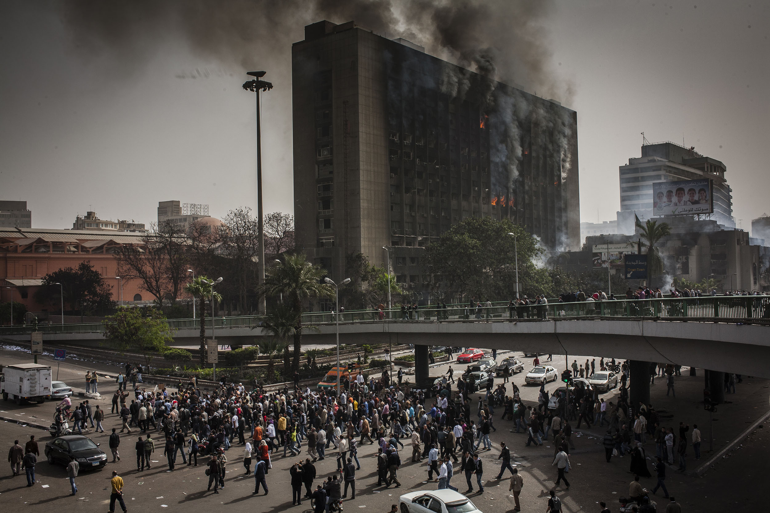  The ruling National Democratic party building burns the morning after being set on fire as protesters gather beneath.  