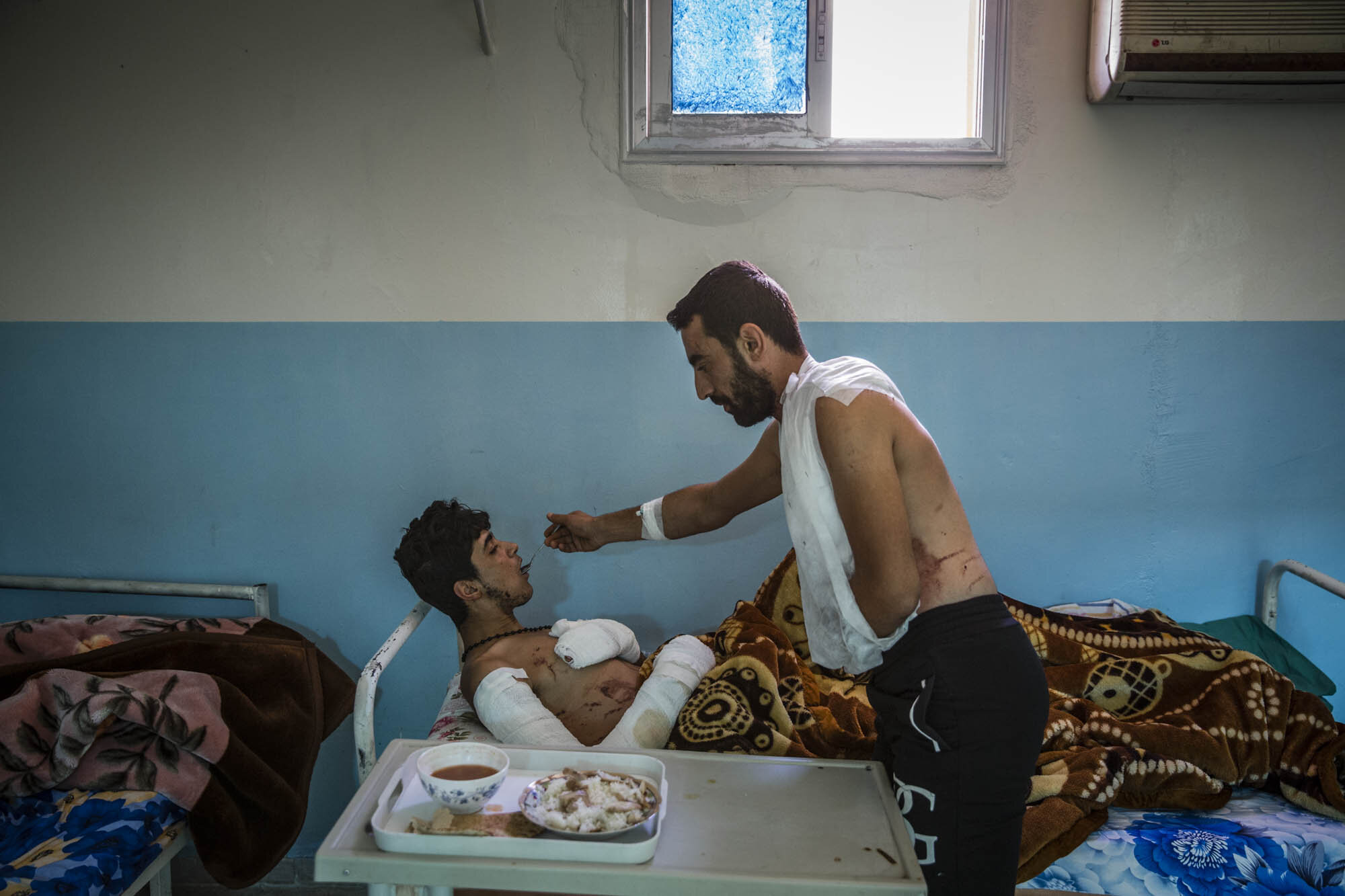  25-year-old Mohammed Sheko fed his SDF comrade, 18-year-old Salah Al Raqawi, at a hospital for injured fighters in Kurdish controlled Syria. The men were both injured in the previous week while fighting ISIS in Raqqa. Syria - Oct 2017 