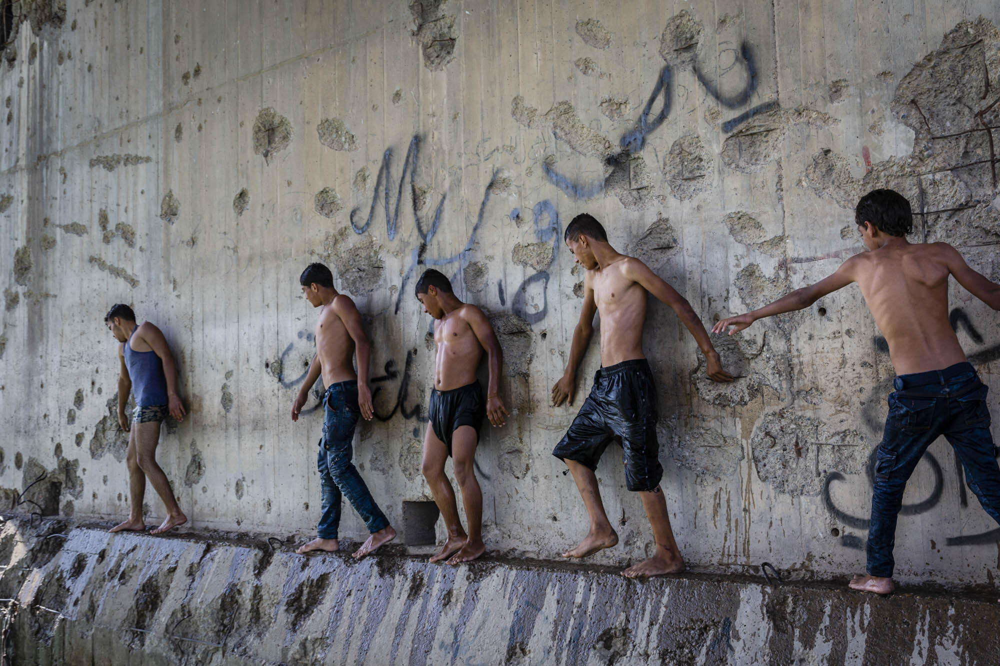  Young boys cooled off in the summer heat in the Euphrates river, under a destroyed bridge in Raqqa. The river borders the South of the city and the only two bridges are still destroyed after being bombed during the operation to defeat ISIS. Syria - 