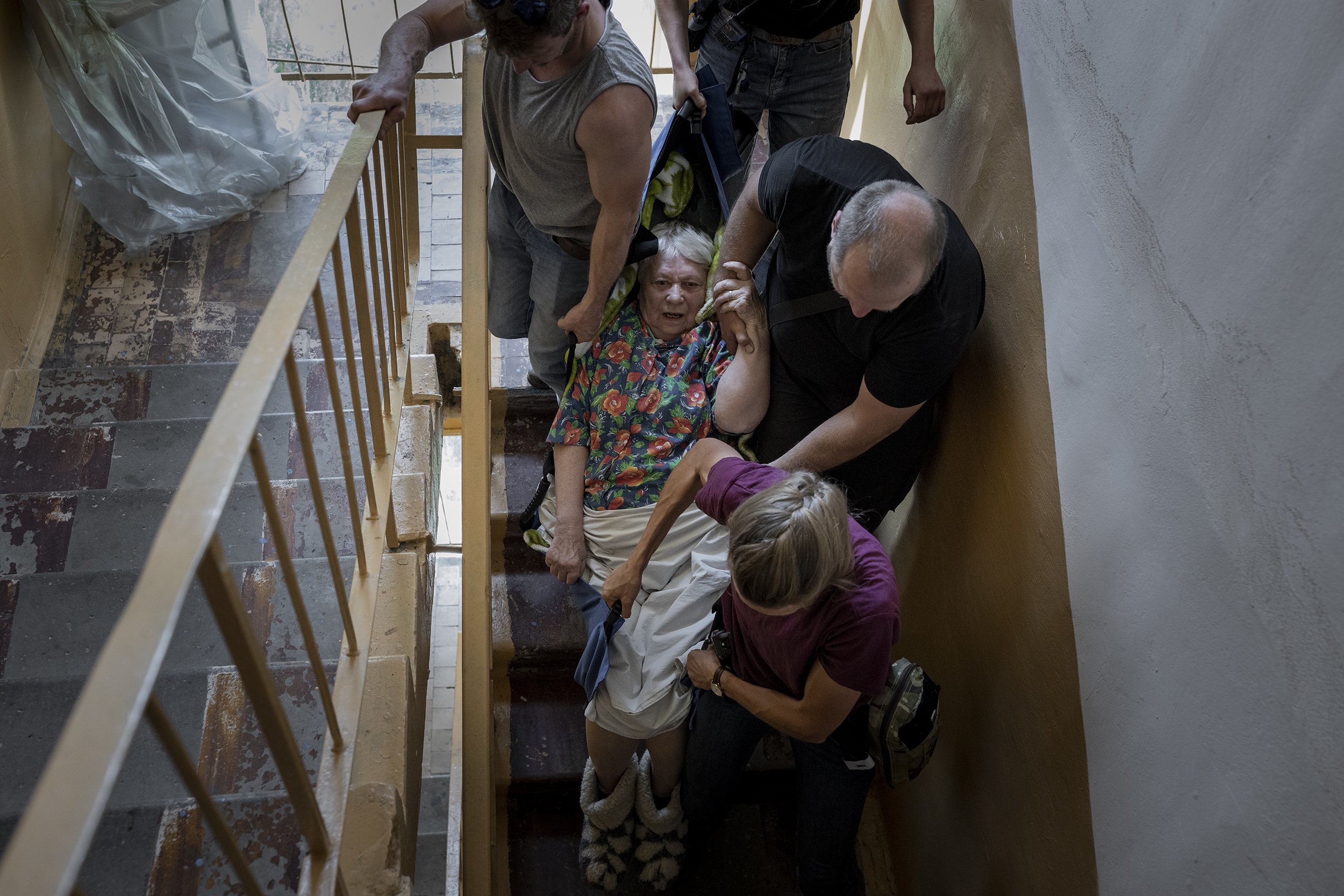  Volunteers from Britain and Ukraine working with the aid organisation Vostok-SOS carried Zinaida Riabtseva, who is 77, blind and struggled to walk down five flights of stairs, during an evacuation mission in Bakhmut. May, 2022. 
