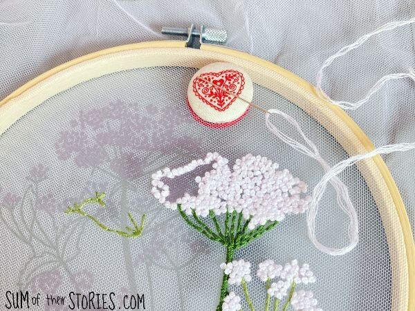 A red heart covered button needle minder on a floral embroidery hoop