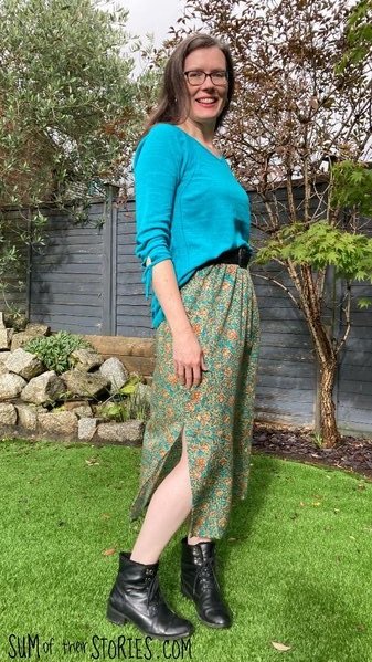 A white woman wears a long straight skirt made from floral brown and turquoise vintage fabric . The skirt has a side split and an elasticated waist band.