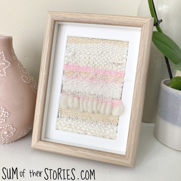 A pink and cream woven tapestry in a frame
