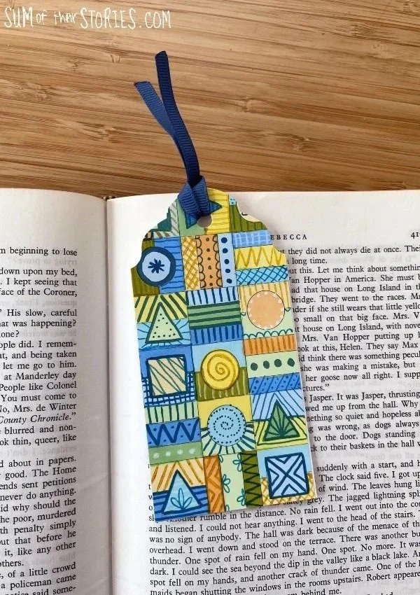 bookmark made from an old colouring page in shades of yellow, blue and green on top of a book page