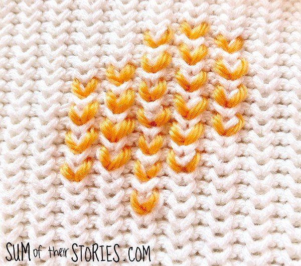 simple swiss darning in orange on a cream sweater