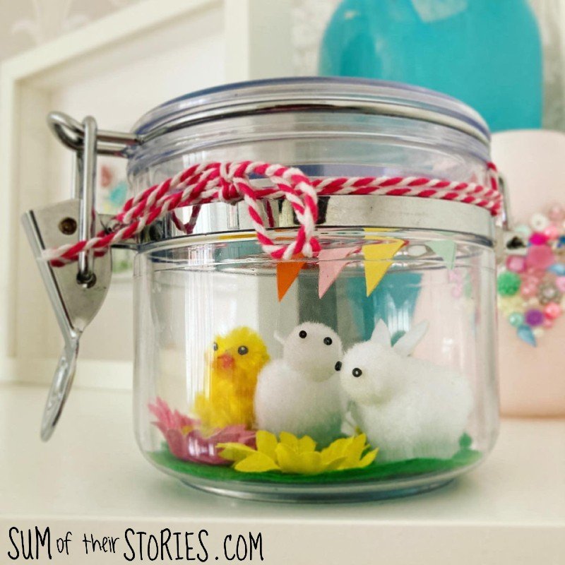a sweet spring scene made in a glass jar with little bunnies and a chick with flowers and mini buntinf
