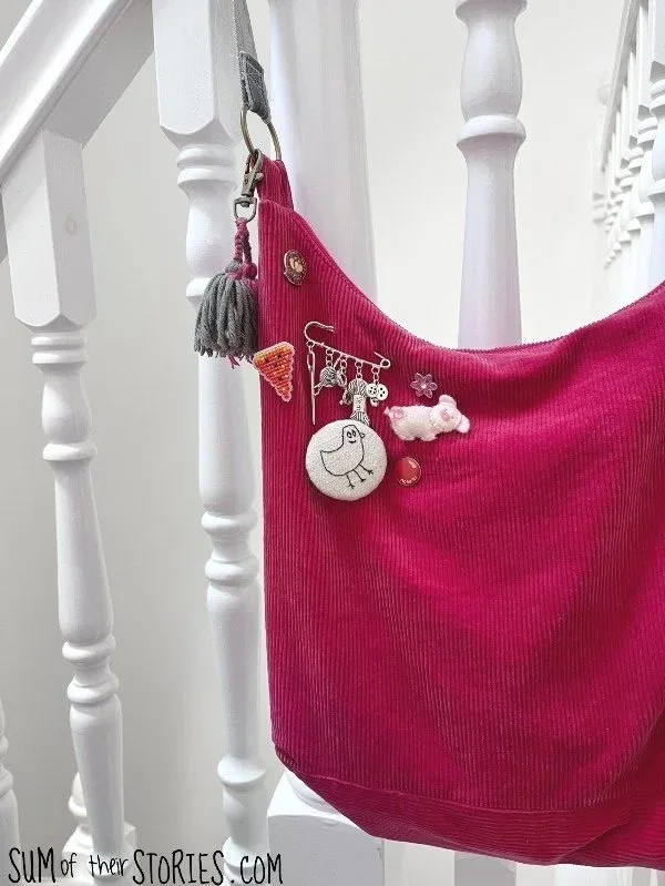 pink bag hanging on bannister with lots of badges including an embroidered duck pin