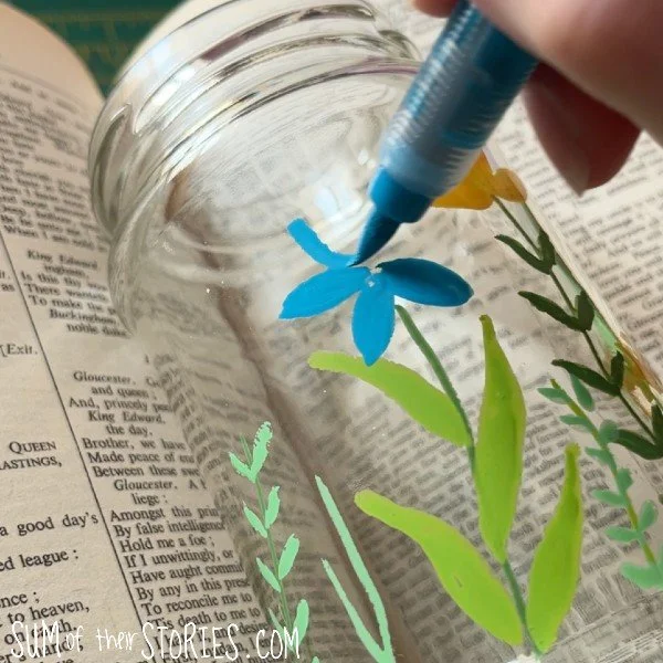 painting a blue flower on a glass jar with acrylic paint pens