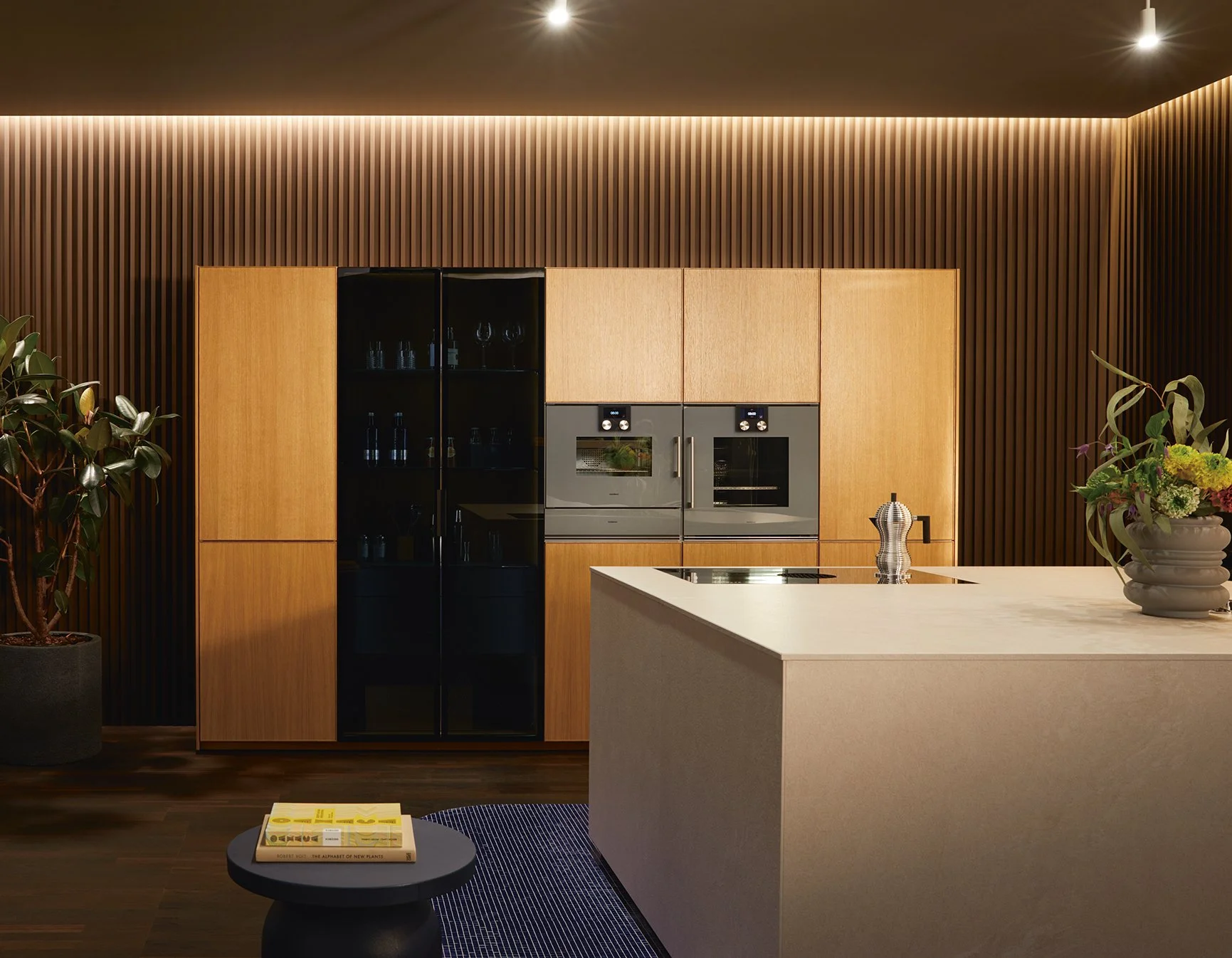 Modern next125 kitchen with reeded grooved oak tall cabinets, black glass display cabinet, built-in ovens, Ceramic bianco beige island