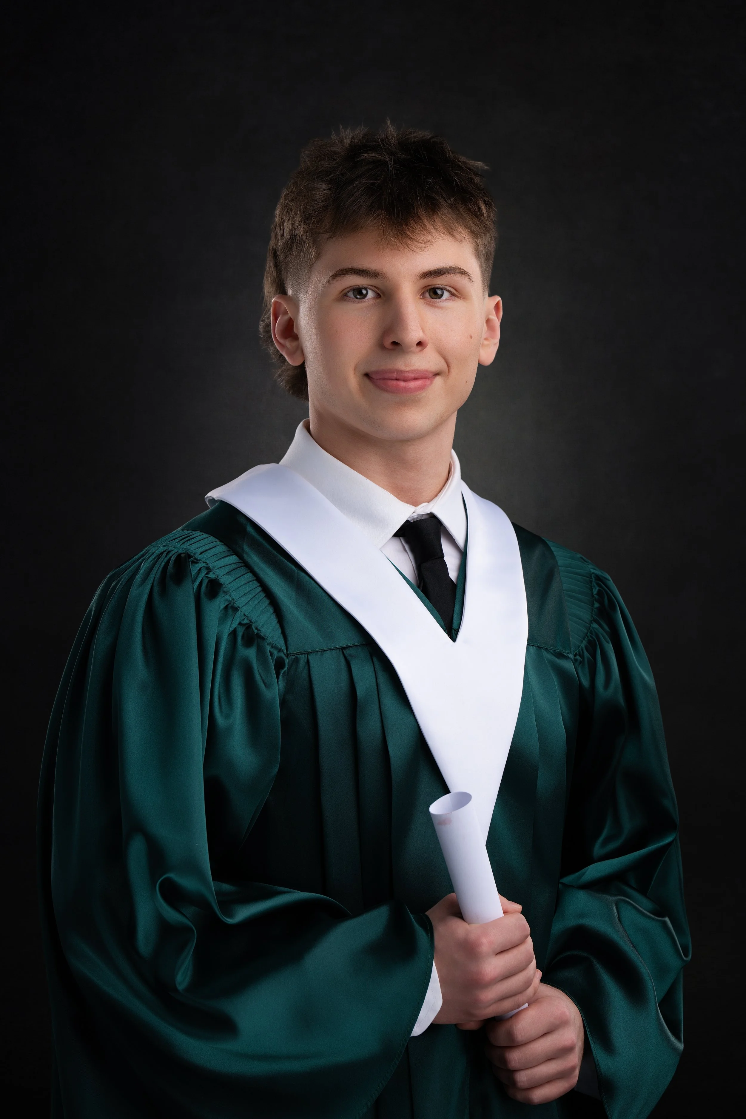 Young man from Memorial High School in graduation gown holding diploma with a dark background.
