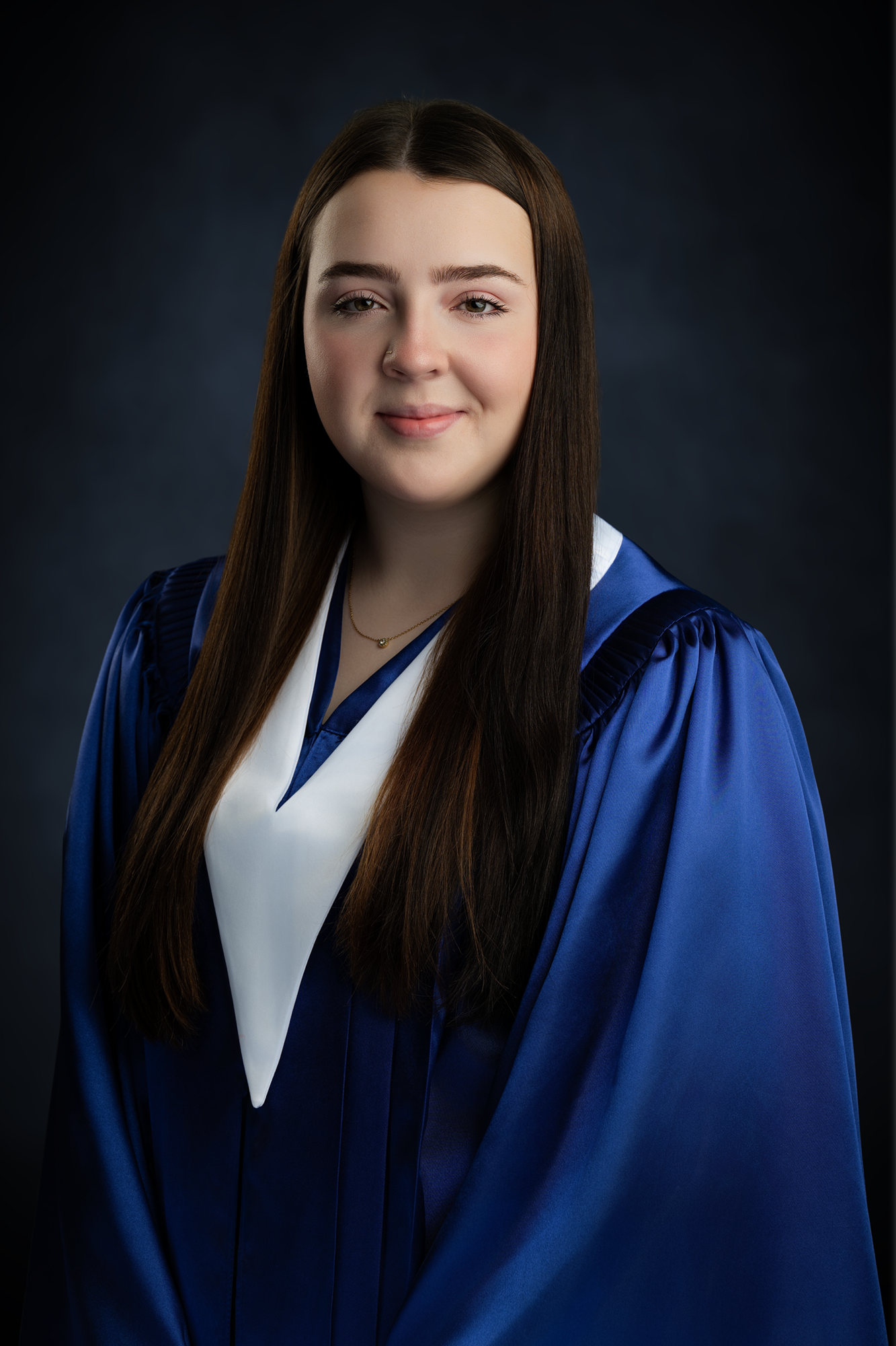 Young woman in a graduation gown and stole, with long brown hair, smiling subtly, against a dark background.