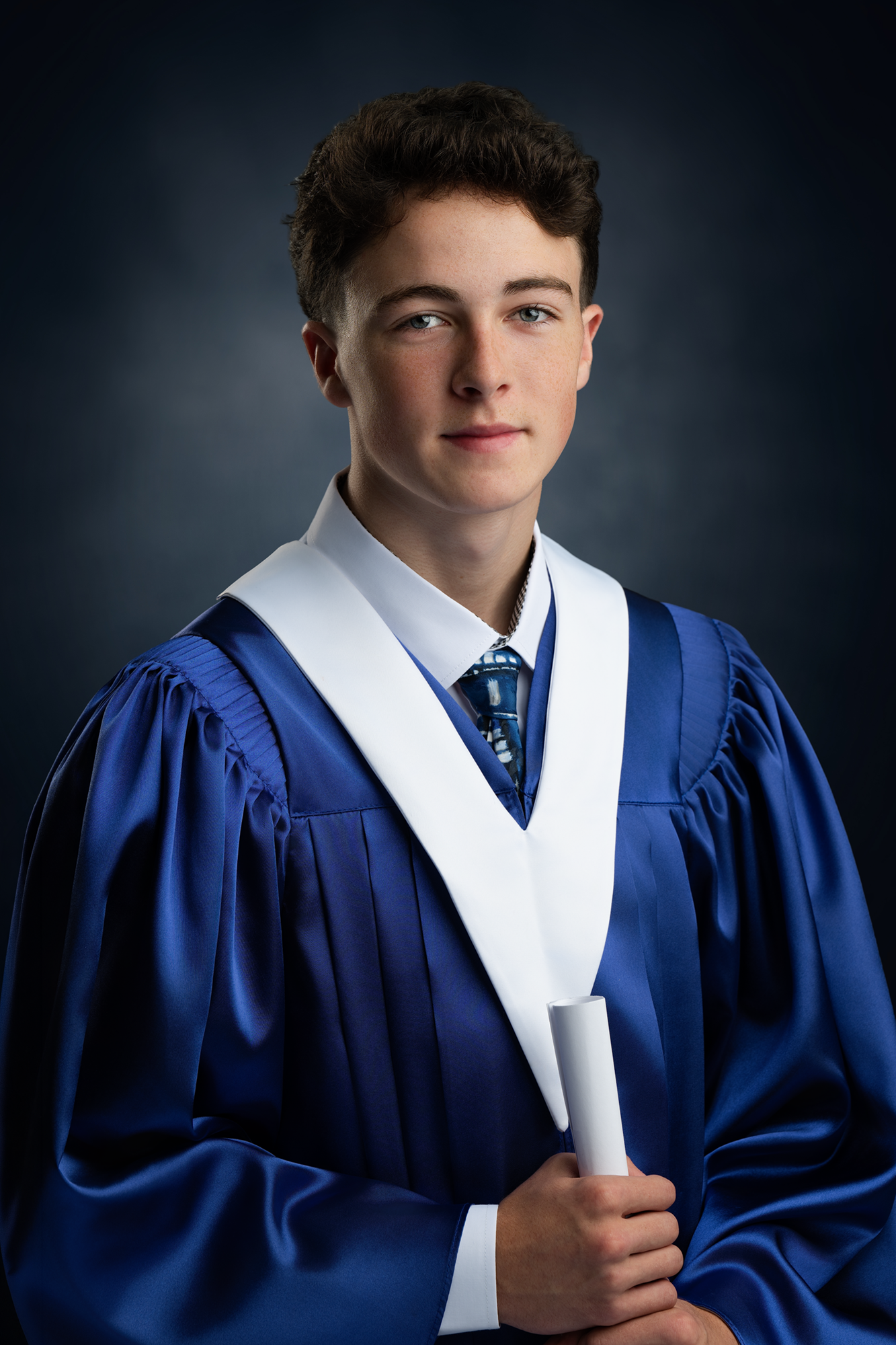 Young man in graduation gown holding diploma, dark background