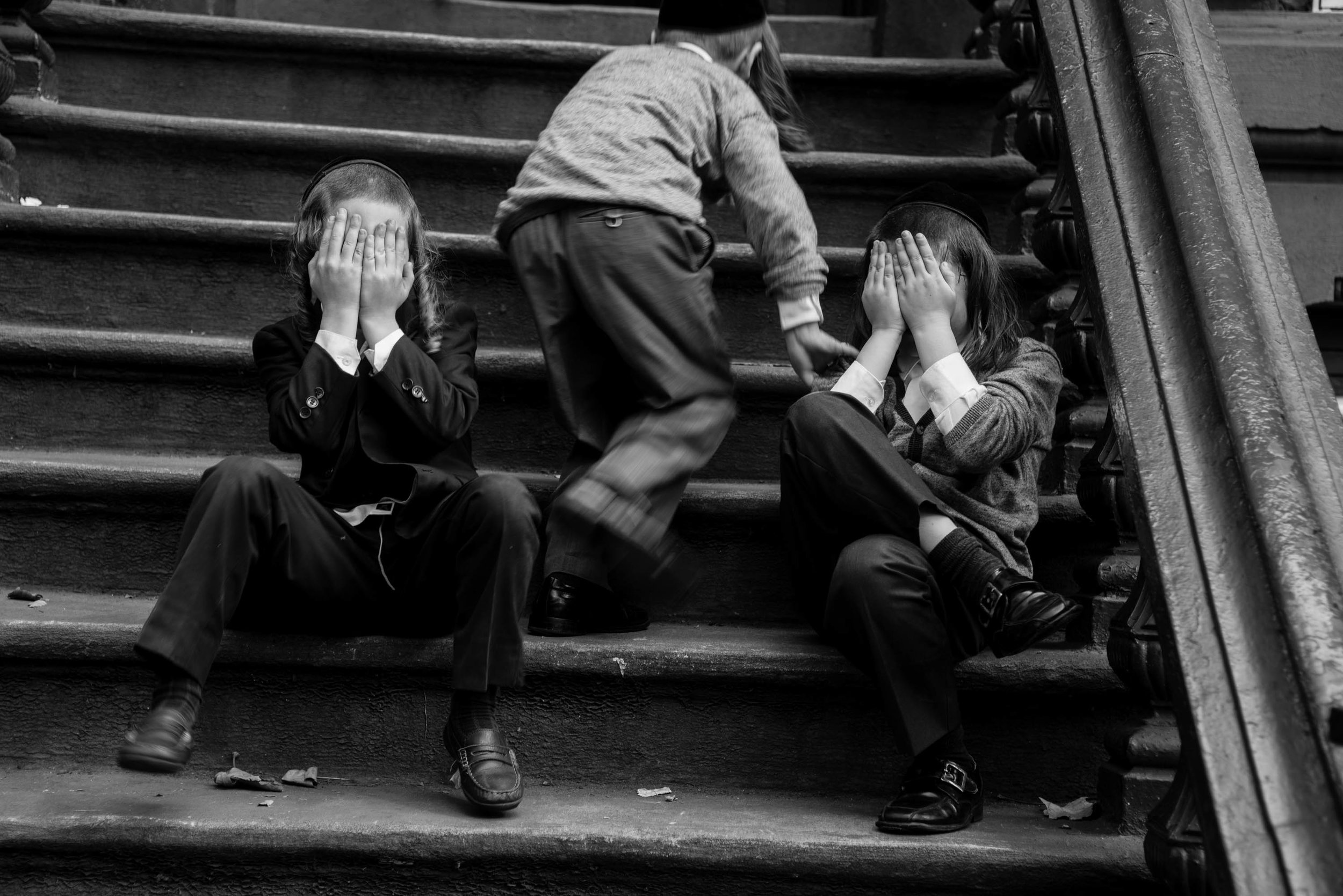 Boys on Steps Hasidic Williamsburg The Satmar Hasid community in Williamsburg, Brooklyn is the most dominant and extreme of the various Hasid sects. I’m drawn to this group of people partly because of my own heritage. As a child I had relatives that lived in Williamsburg and on the infrequent occasions when I visited the community with my parents I was fascinated by their unfamiliar way of life. The dialectical nature of life intrigues me. The people who live in Williamsburg are frequently described as unfriendly and harsh. I have wanted to understand the seeming incongruence of how these very serious and private people can in an instant burst into spirited and sometimes rapturous celebration. The dichotomies of the Hasid Williamsburg community are reflected in how it’s people live. The community minimizes contact with the external world while simultaneously cherishing and celebrating family ties and worship. The insular and restrictive lifestyle is maintained as a way of preventing the dilution of religion and traditions through contact from outside influence. The old and strict traditions may seem oppressive and exclusive from the outside, but for most Hasids their religion and the codes they live by are a work of love and a source of great joy.