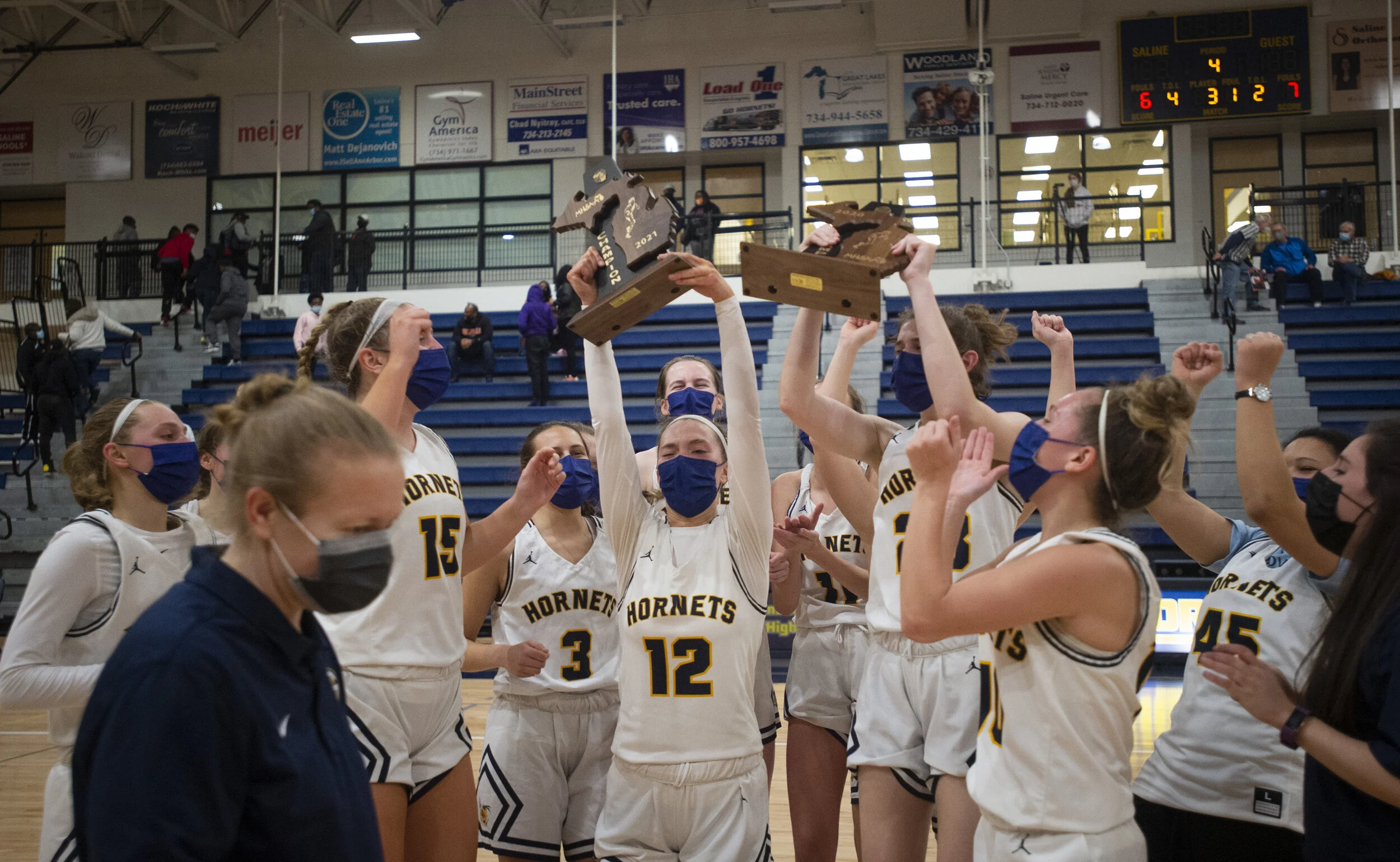  Ella Stemmer (12) holds up the 2021 District Champions trophy after a win against Belleville at Saline and her coach Leigh Ann Roehm, left, smiles after the district championship game on Friday, March 26, 2021. Saline won 64-32 and advanced to regio
