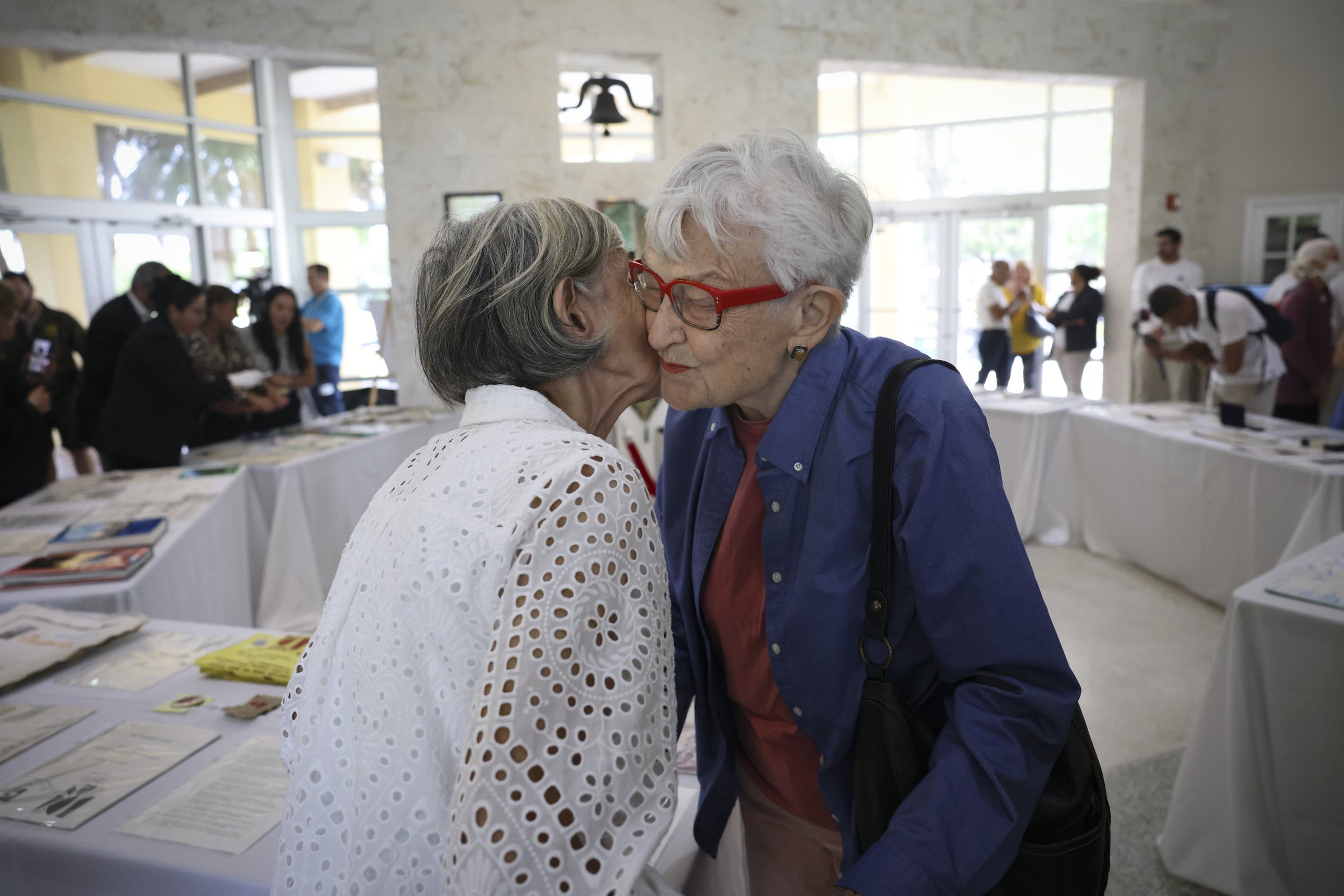 Sylvia Unzueta, a Women’s Park founder, left, kisses Freda Tschumy, the artist who designed the time capsule, during the unveiling of its contents, pictured behind them, from 31 years ago on Wednesday, March 22, 2023, at Women's Park in Miami, Fla. T