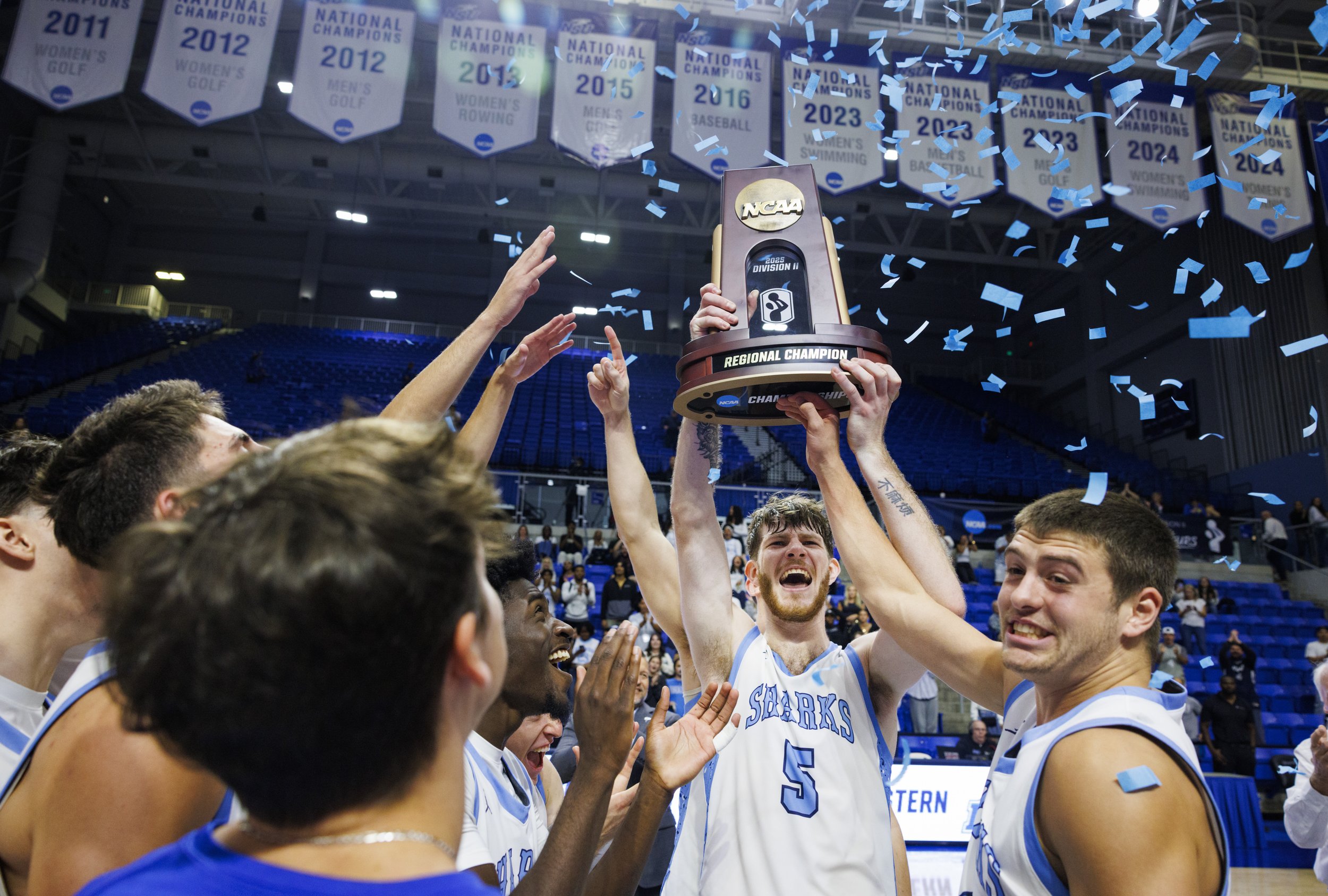 NSU Sharks Ryker Cisarik (5) raises the trophy above his head with NSU Sharks Eli Allen (14) and the rest of the team after winning the NCAA Division II South Regional final against the UAH Chargers on Tuesday, March 18, 2025, in the Rick Case Arena