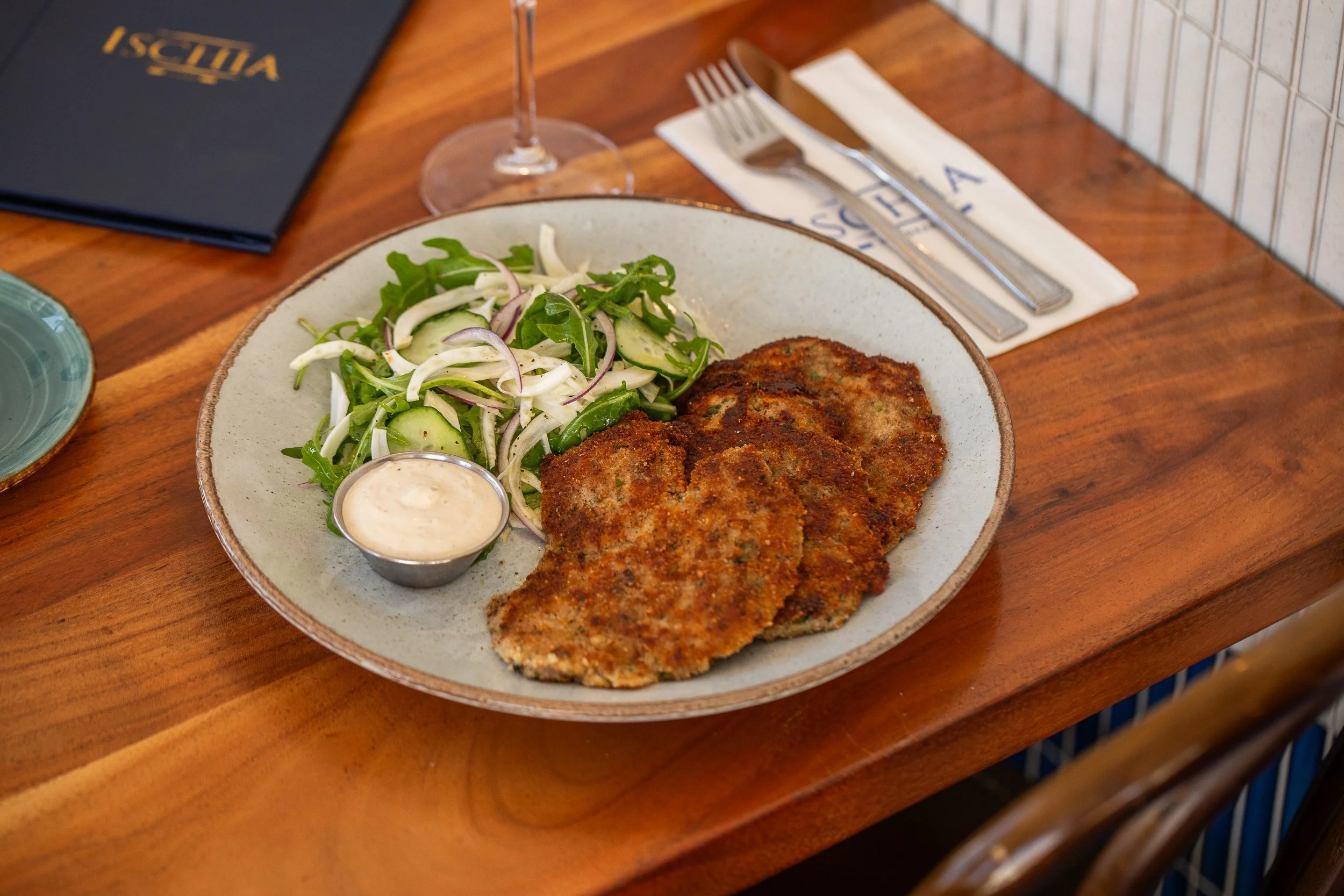 Plate of breaded and fried cutlets served with a side salad and a small cup of dipping sauce at a restaurant.
