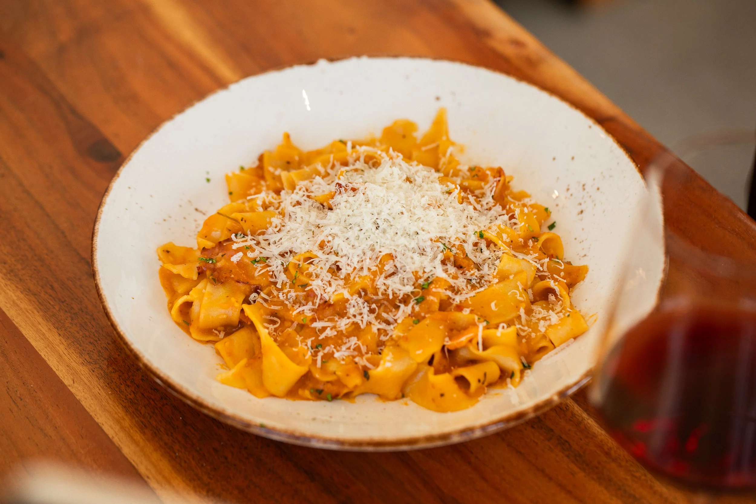 Bowl of pasta with orange sauce topped with grated cheese on a wooden surface.