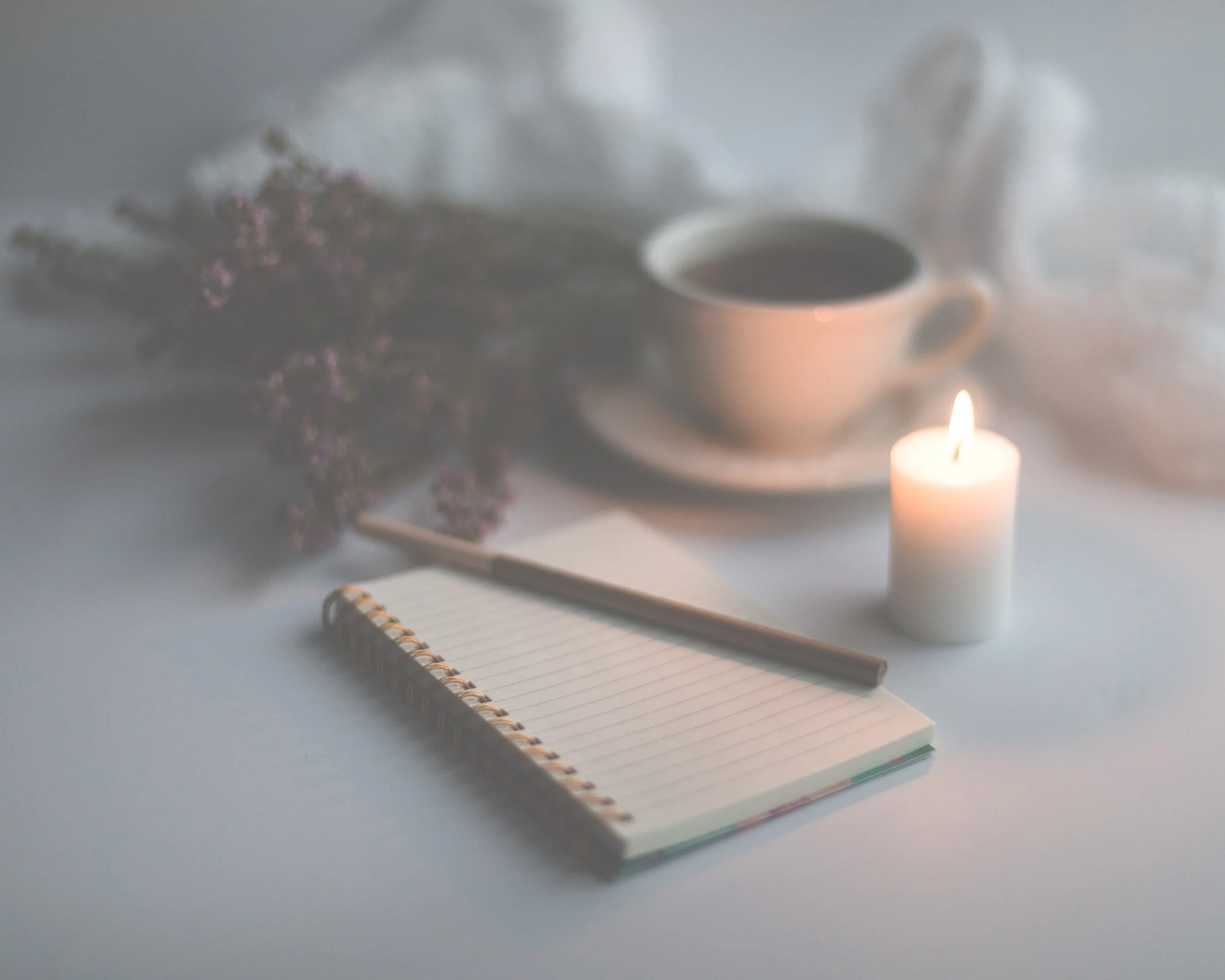 Notepad and pen sitting next to dried flowers and a candle
