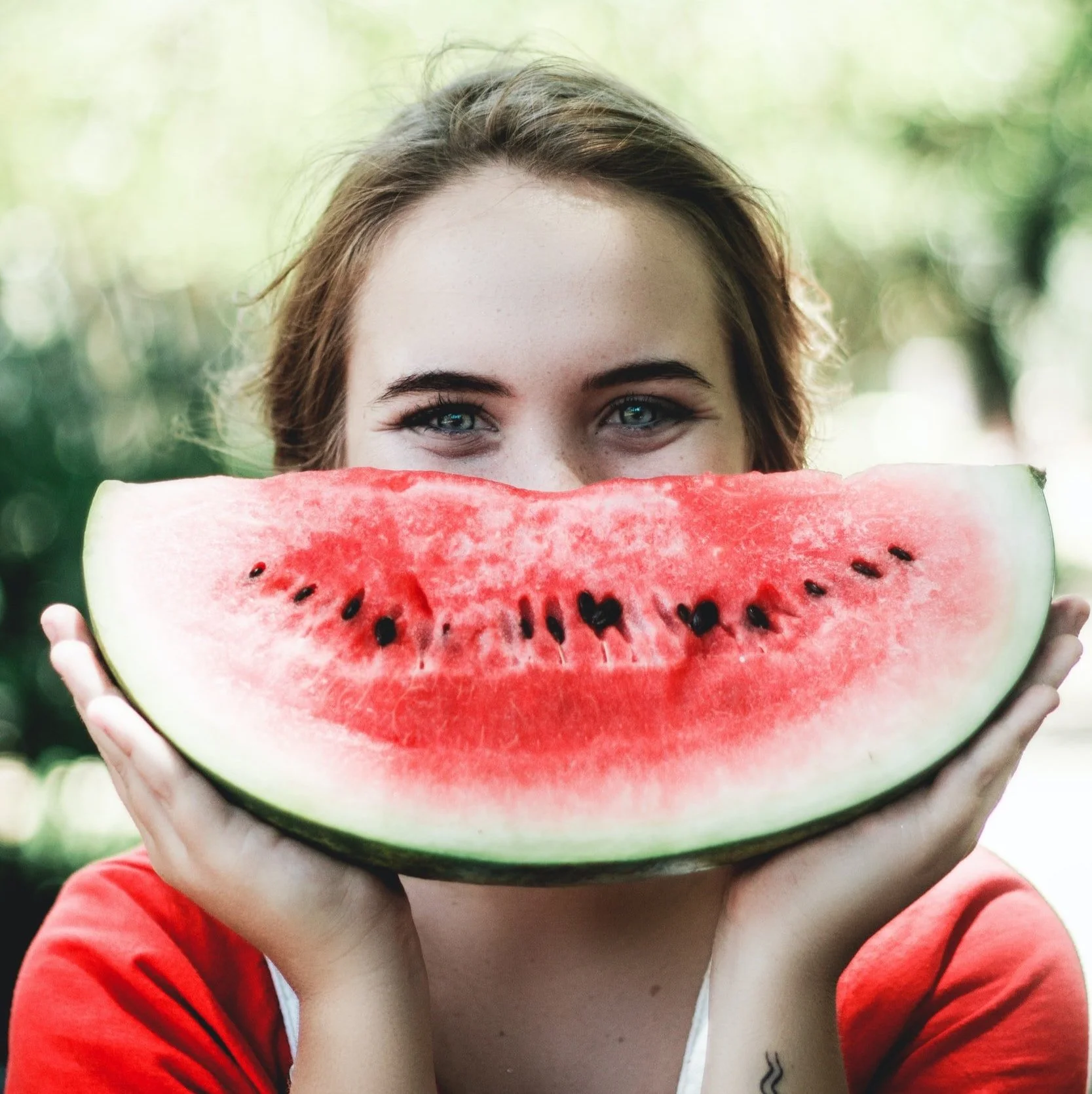 Fair skinned woman holding a wedge of watermelon in front of her mouth like a smile