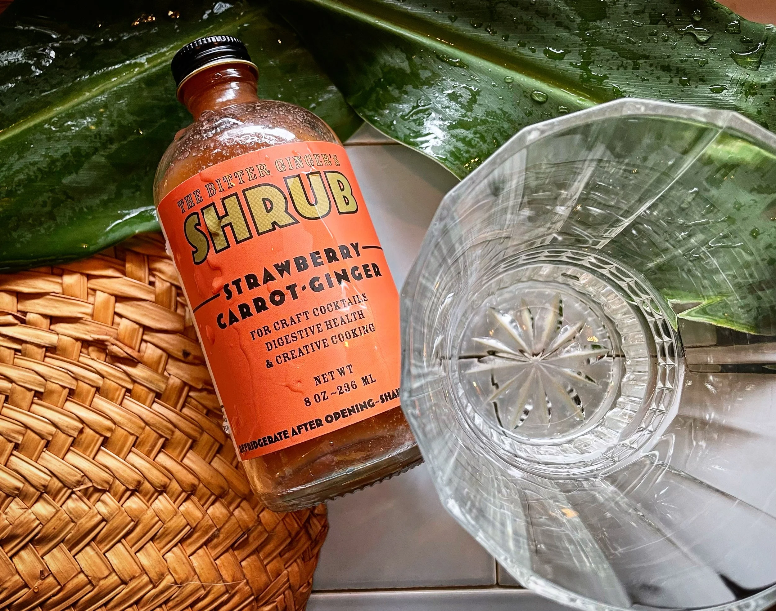 BitterGinger-Shrubs-StrawberryCarrotGingerShrub-BottleBesideCocktailGlass-FanGingerLeaf-20240131.JPG