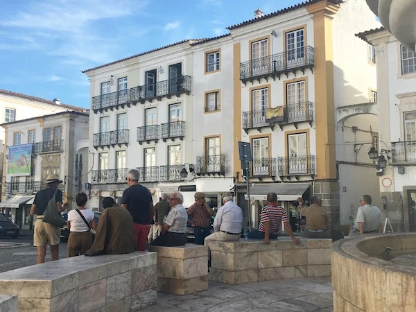 Local residents and tourists sitting on the fountain area in the middle of the square in Evora, Portugal